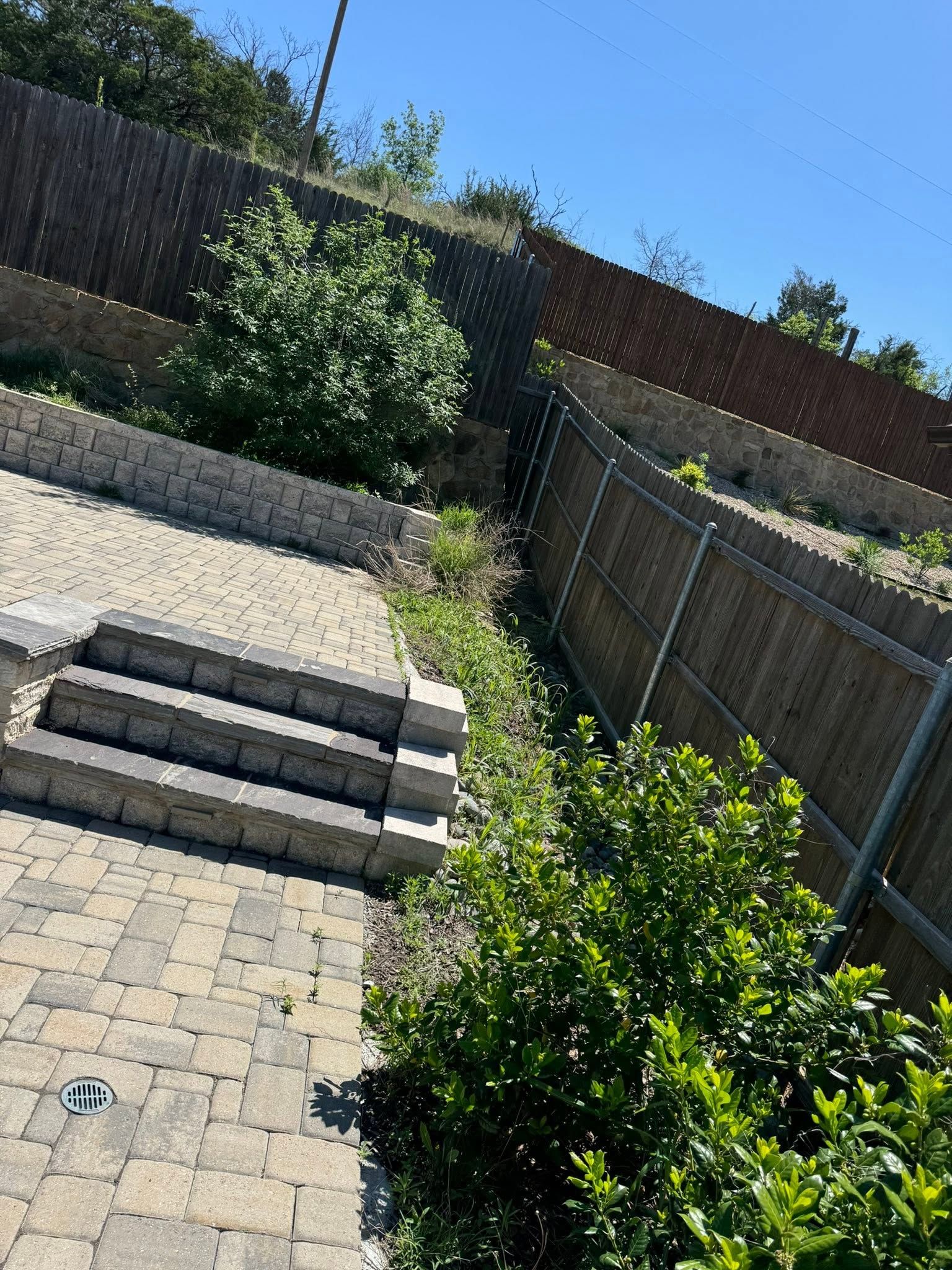 Sloped backyard patio with stone steps, gravel path, and green shrubs under a blue sky