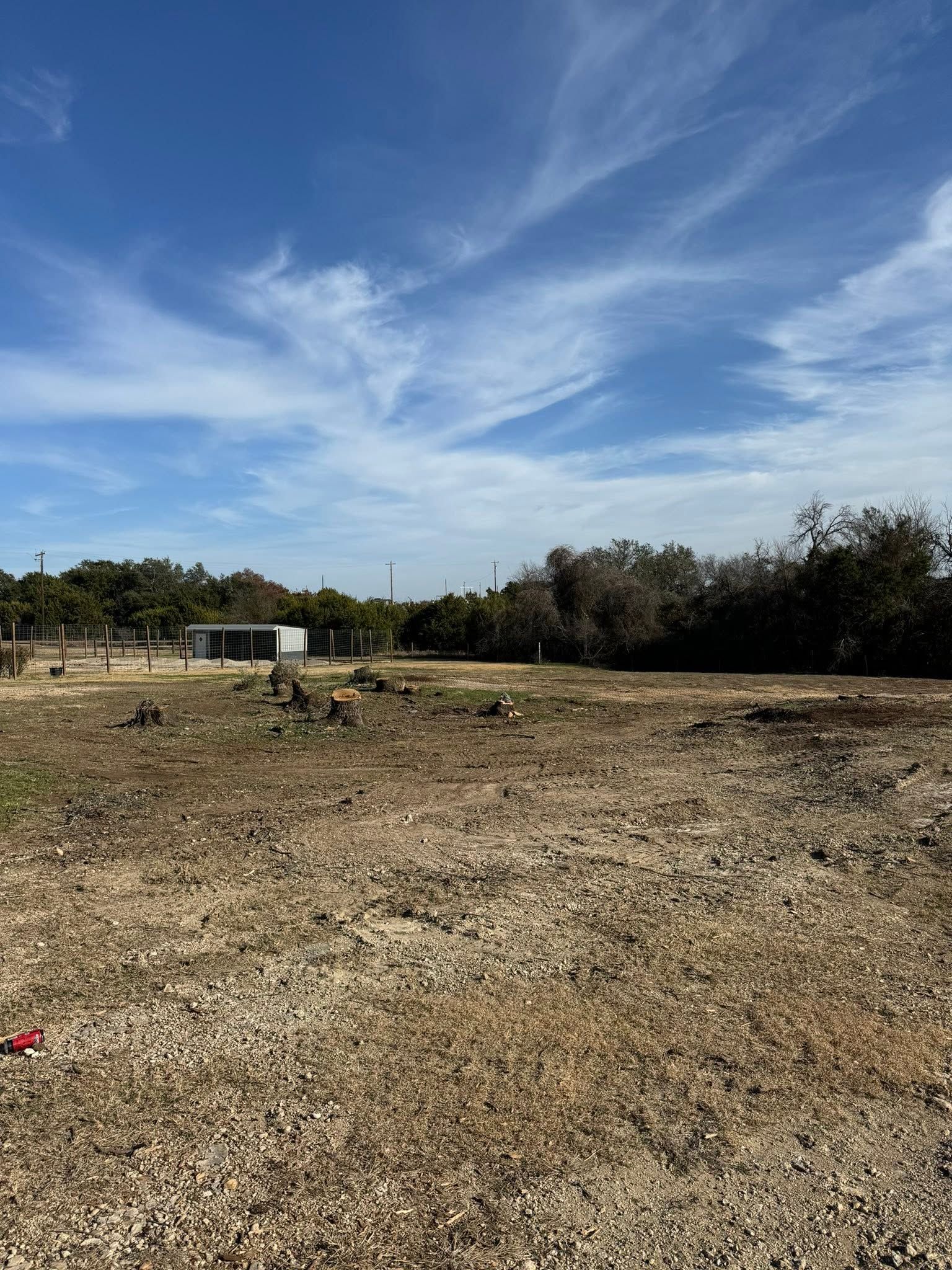 Dry, rocky field under a bright blue sky with wispy clouds and a small white trailer in the distance