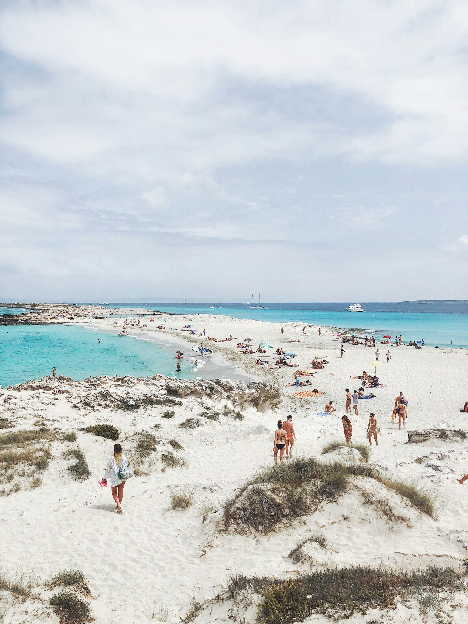 En gruppe mennesker går på en sandstrand nær havet.