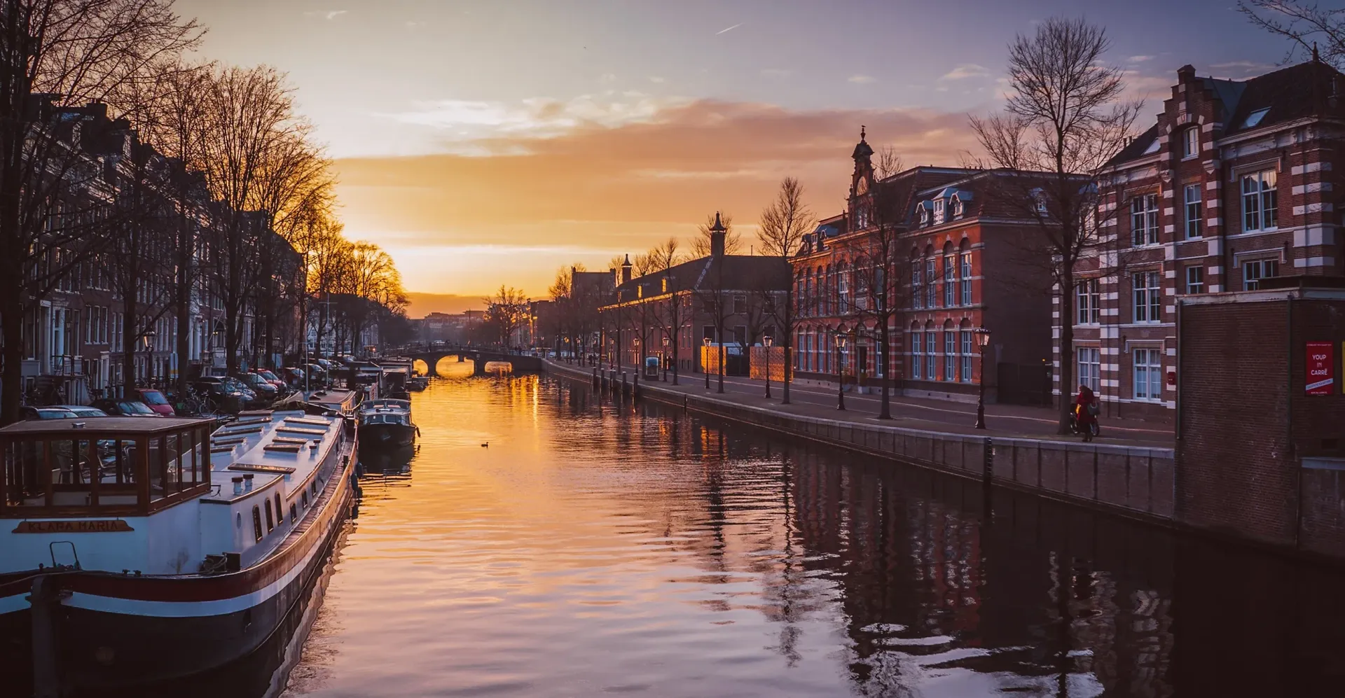 En kanal i amsterdam med båter og bygninger ved solnedgang.