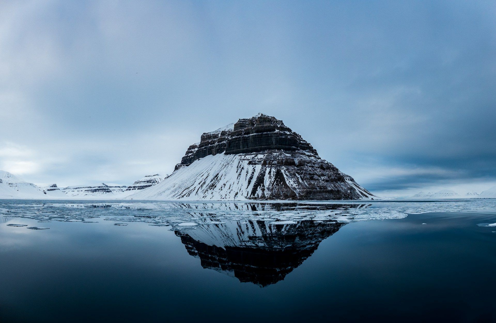 Et snødekt fjell reflekteres i vannet i en innsjø.