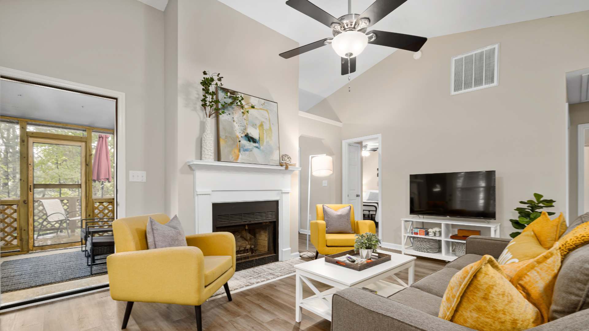 Living room with fireplace, yellow chairs, gray couch, and TV. A doorway leads to a screened porch.