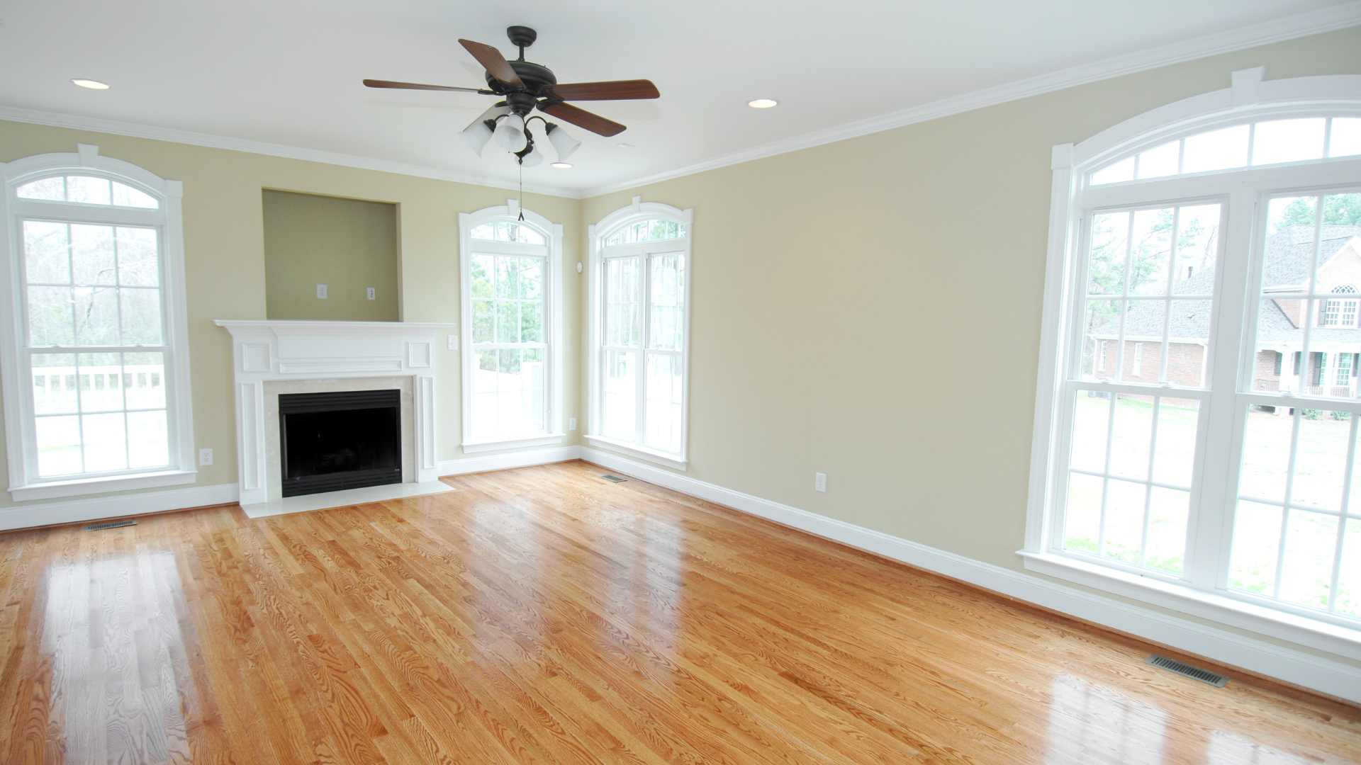 Empty room with hardwood floors, fireplace, arched windows, and ceiling fan.