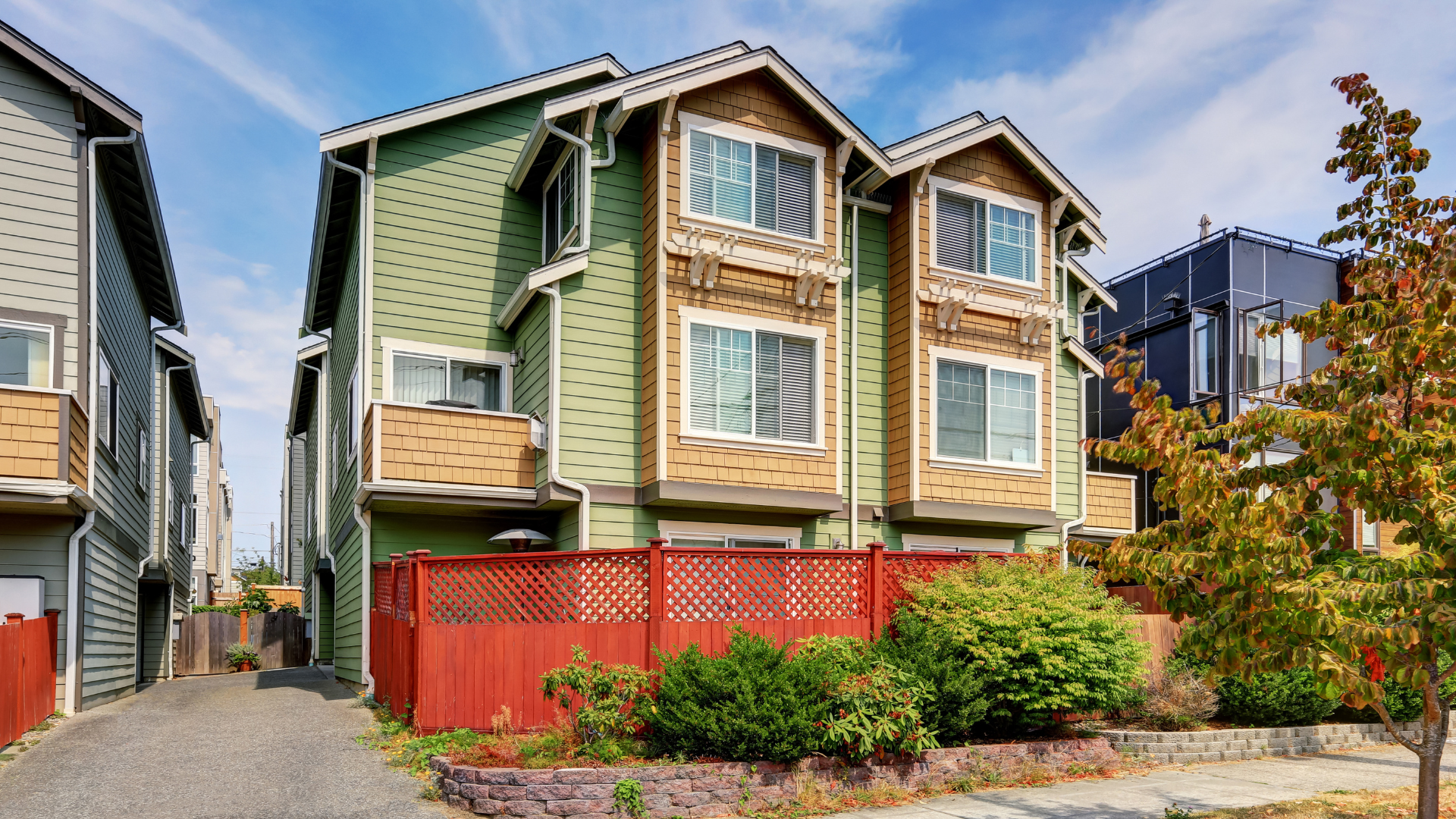 Green and brown multi-story townhouses with red fence and sunny sky.