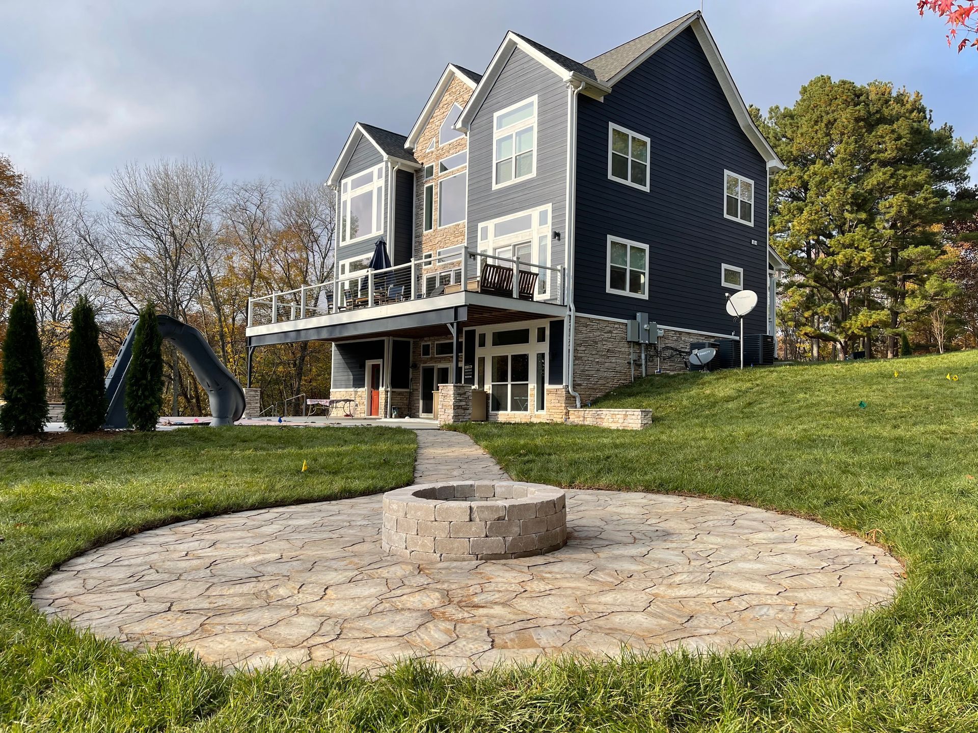 Large dark blue house with white trim and a stone circular patio in a grassy yard