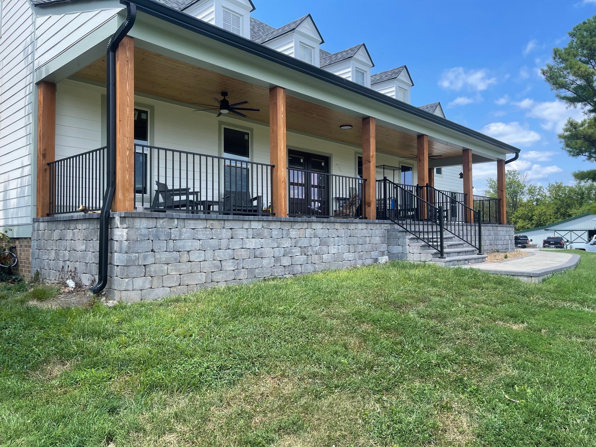 Stone building with a covered porch, black railings, and grassy lawn under a blue sky