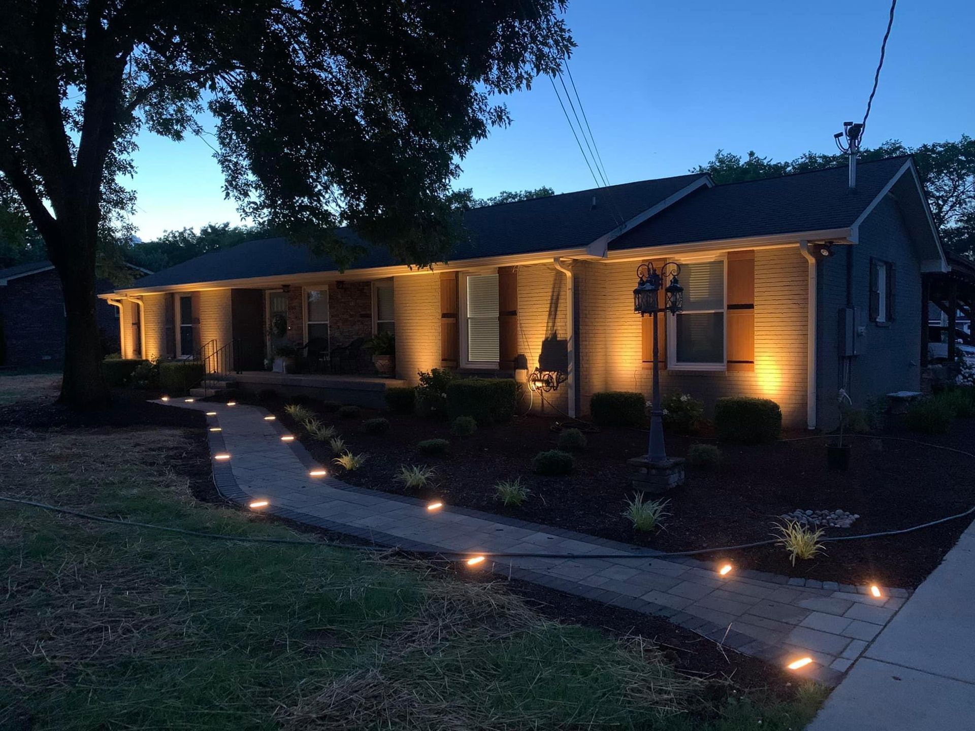 Single-story house at dusk with warm porch lights and a lit curved walkway
