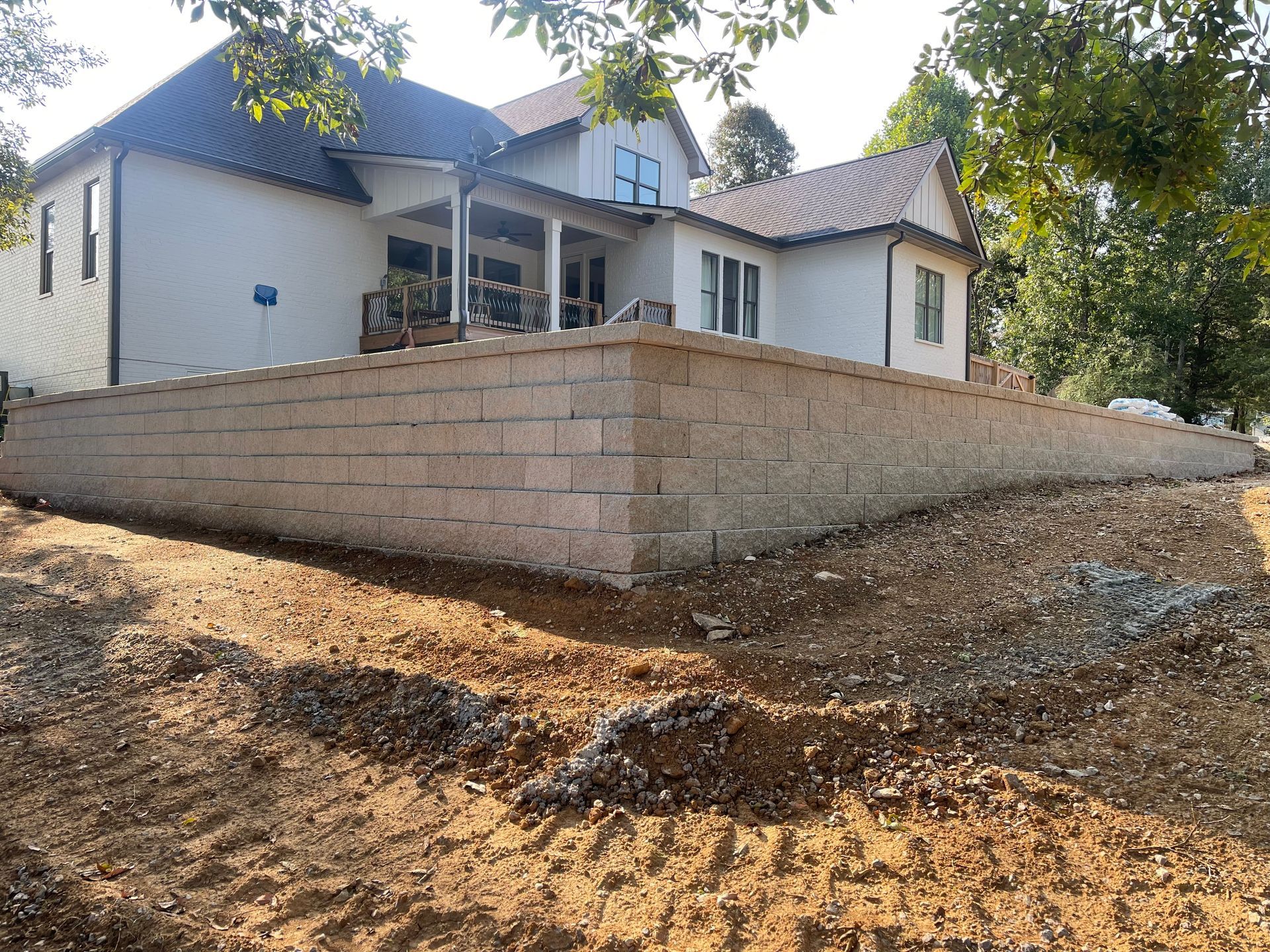 House on a raised concrete retaining wall on a dirt hillside under trees
