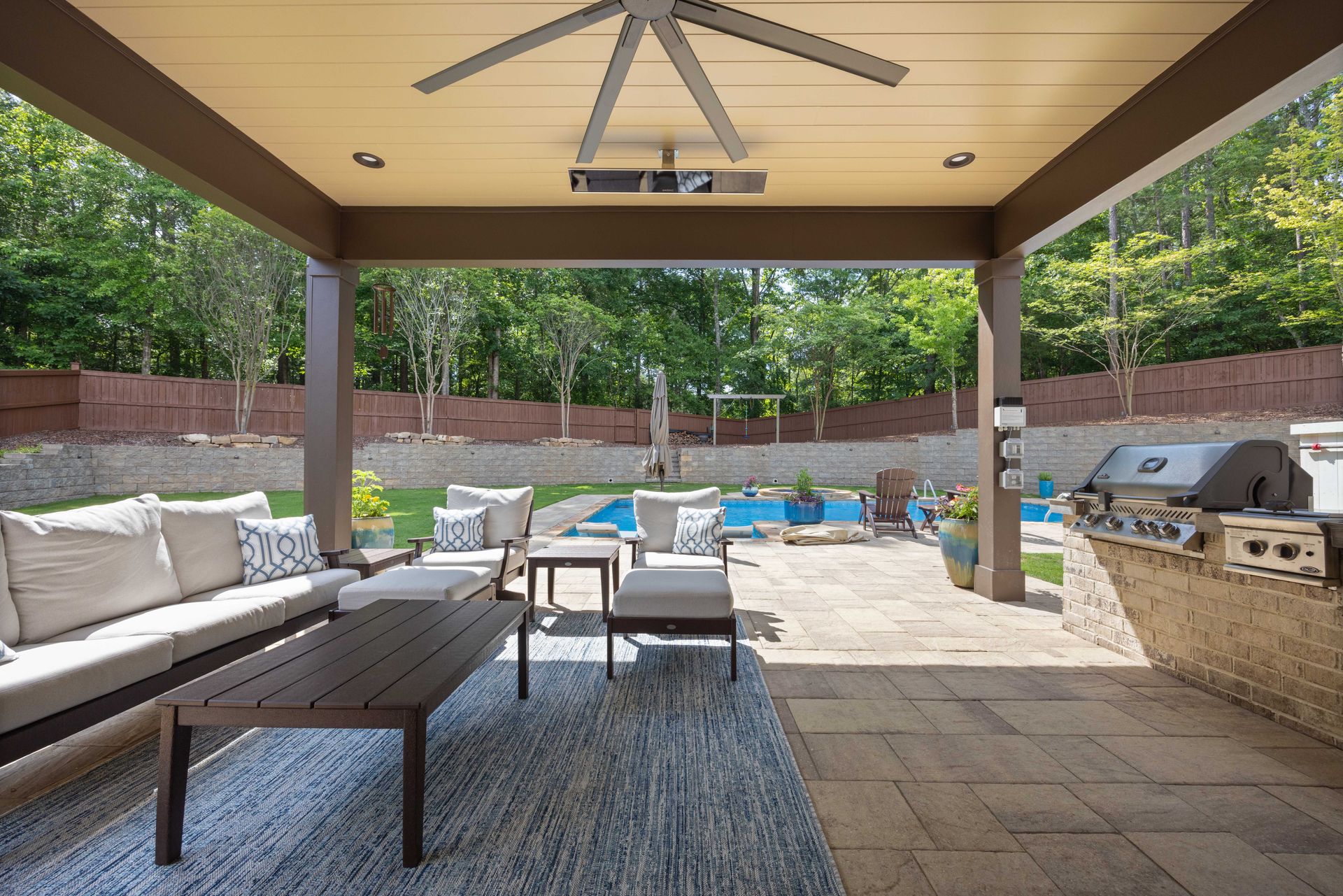 Covered patio with outdoor seating, rug, grill, and pool view in a landscaped backyard.