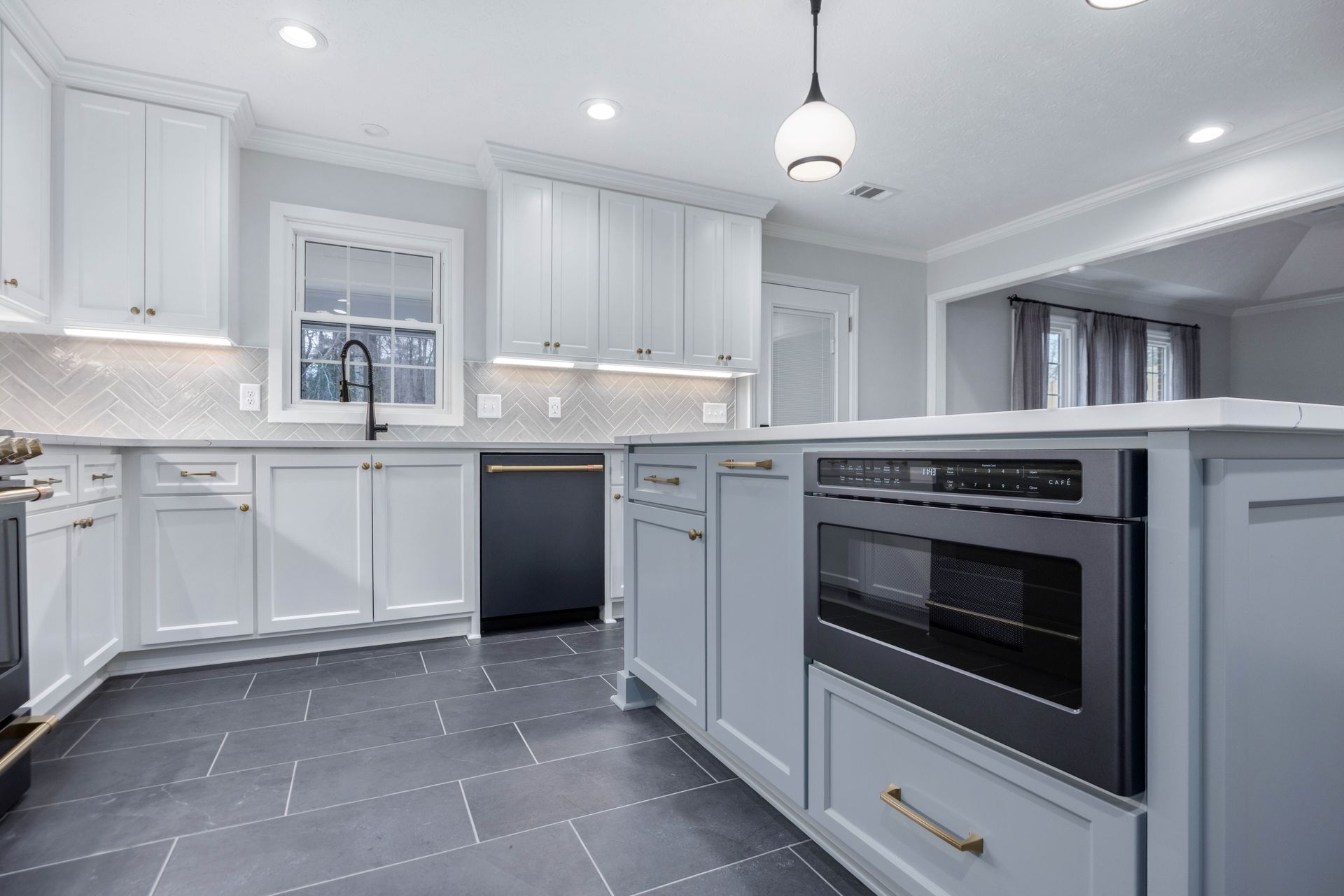 Bright modern white kitchen with gray cabinets, black countertop, and built-in oven
