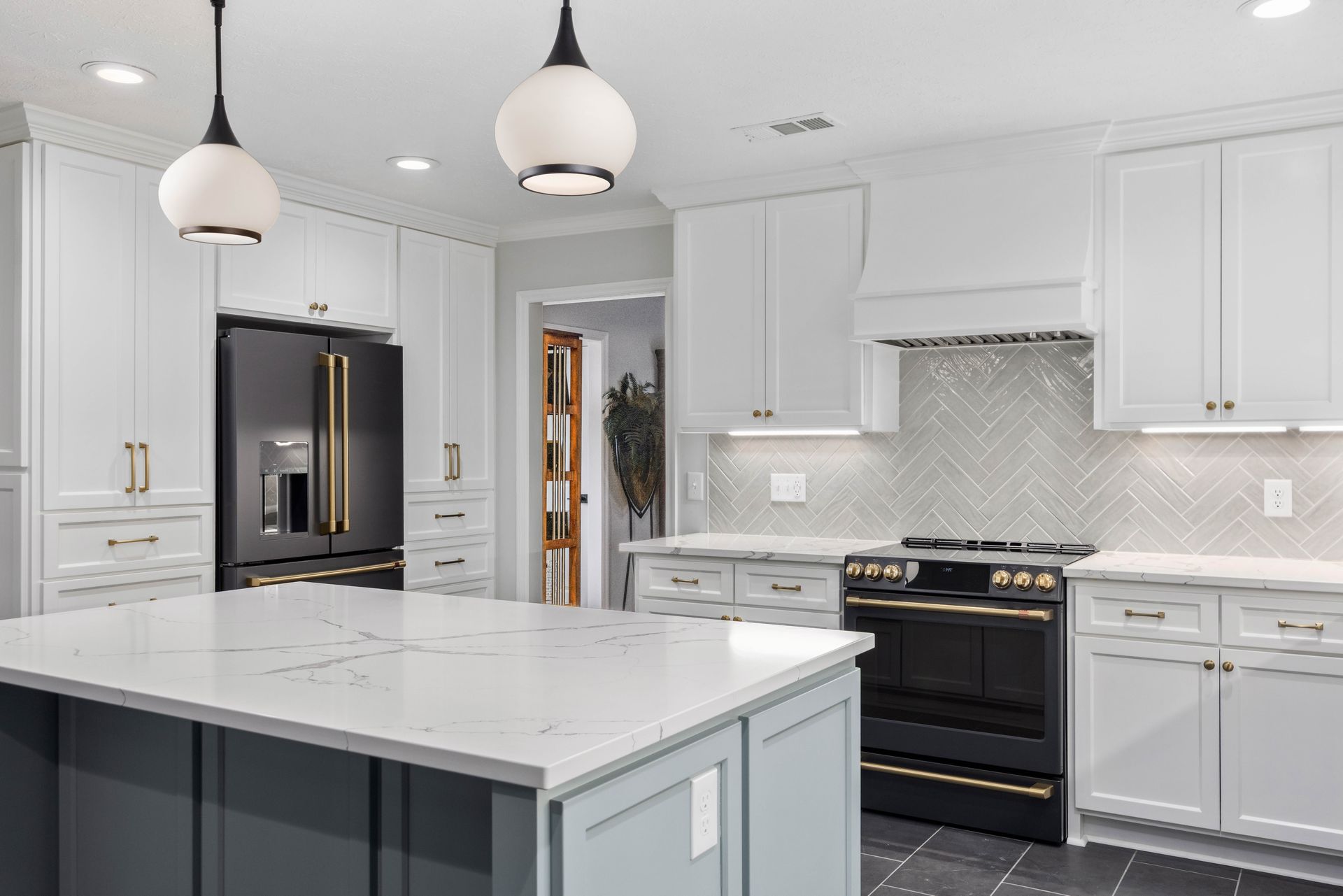 Modern white kitchen with marble island, black appliances, and pendant lights