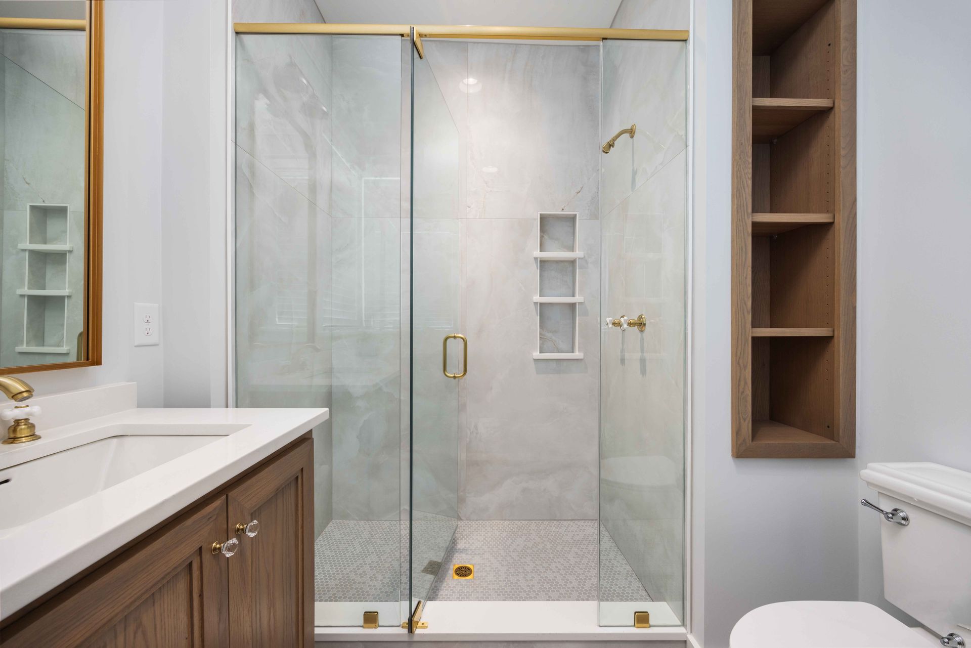 Modern bathroom with glass shower, white tile, wood vanity, and toilet