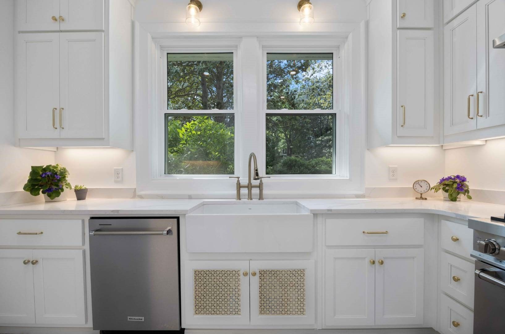 Bright white kitchen with a centered window, sink, and stainless dishwasher under cabinets