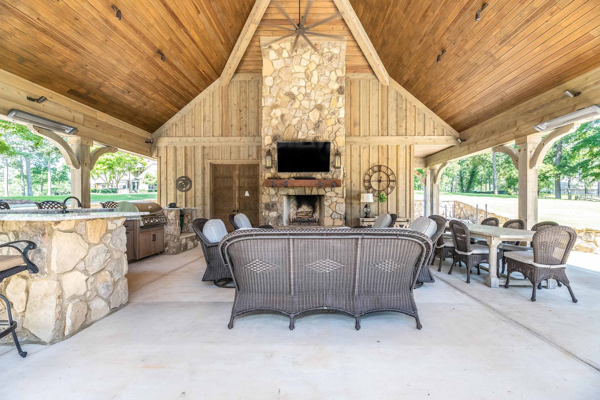 Stone pavilion patio with wicker seating, fireplace, and vaulted wood ceiling