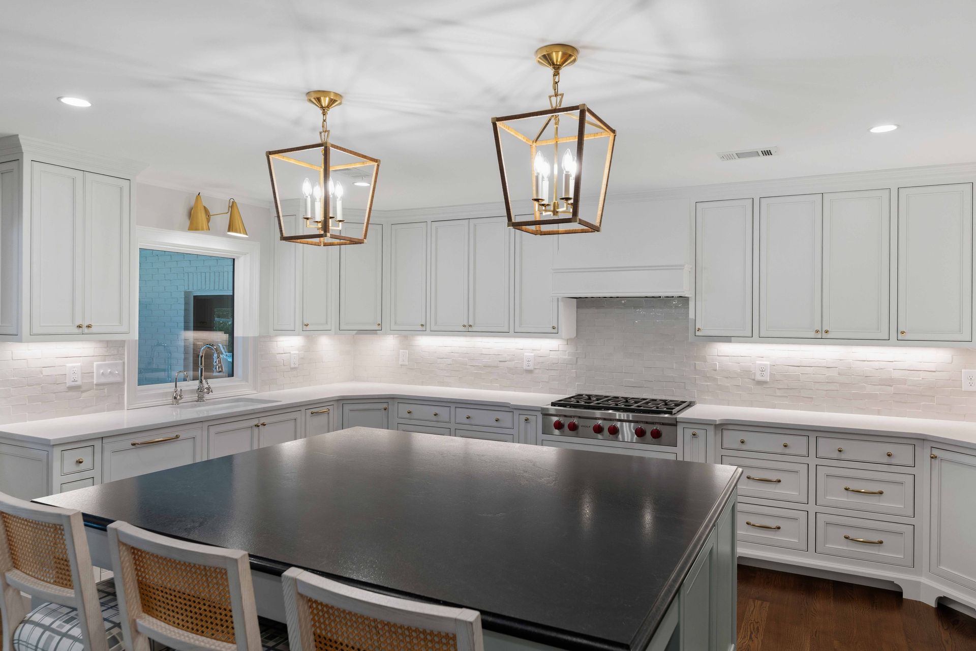 Bright white kitchen with marble counters, dark island, and brass pendant lights