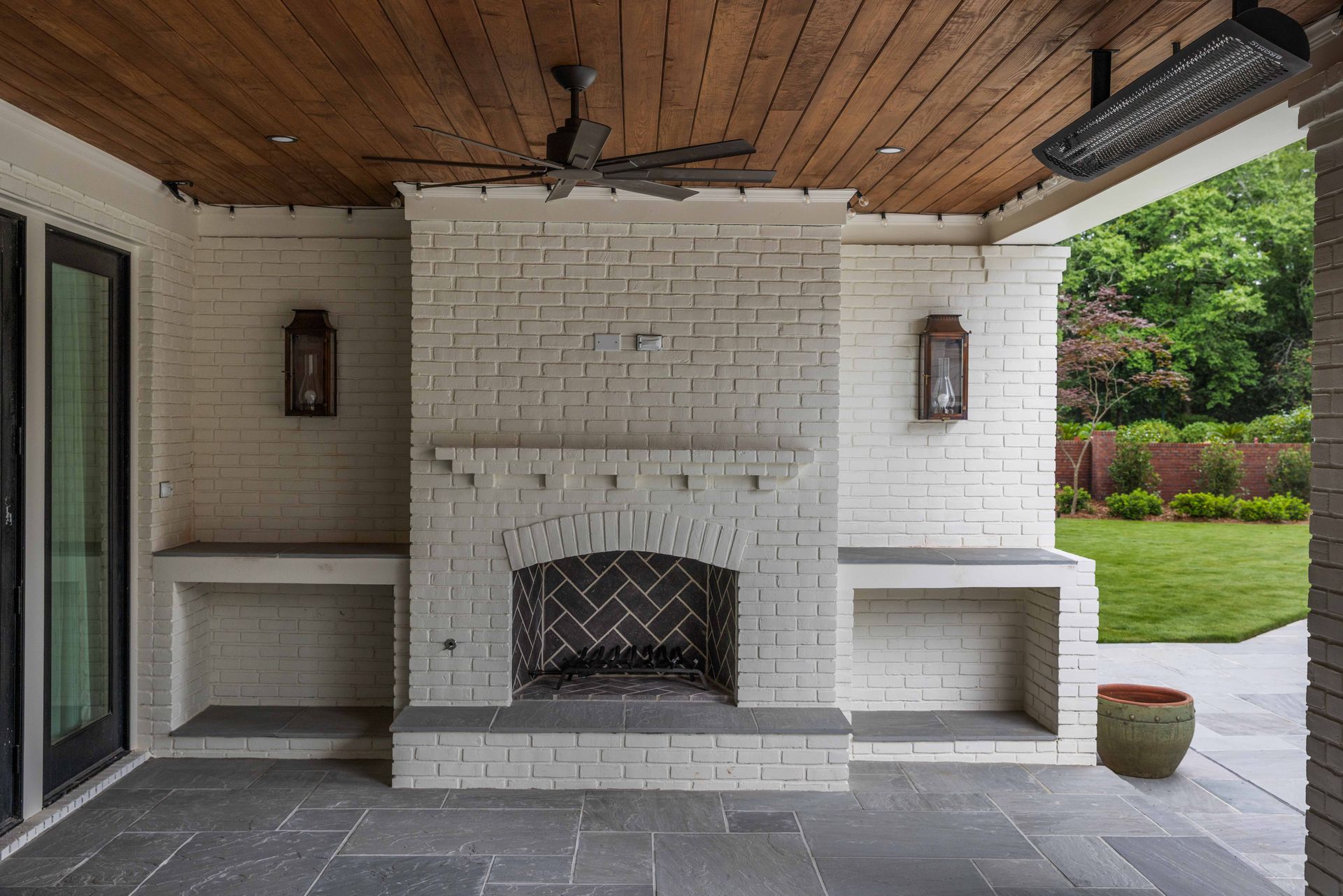 Covered patio with white brick fireplace, built-in benches, and a wood-paneled ceiling.