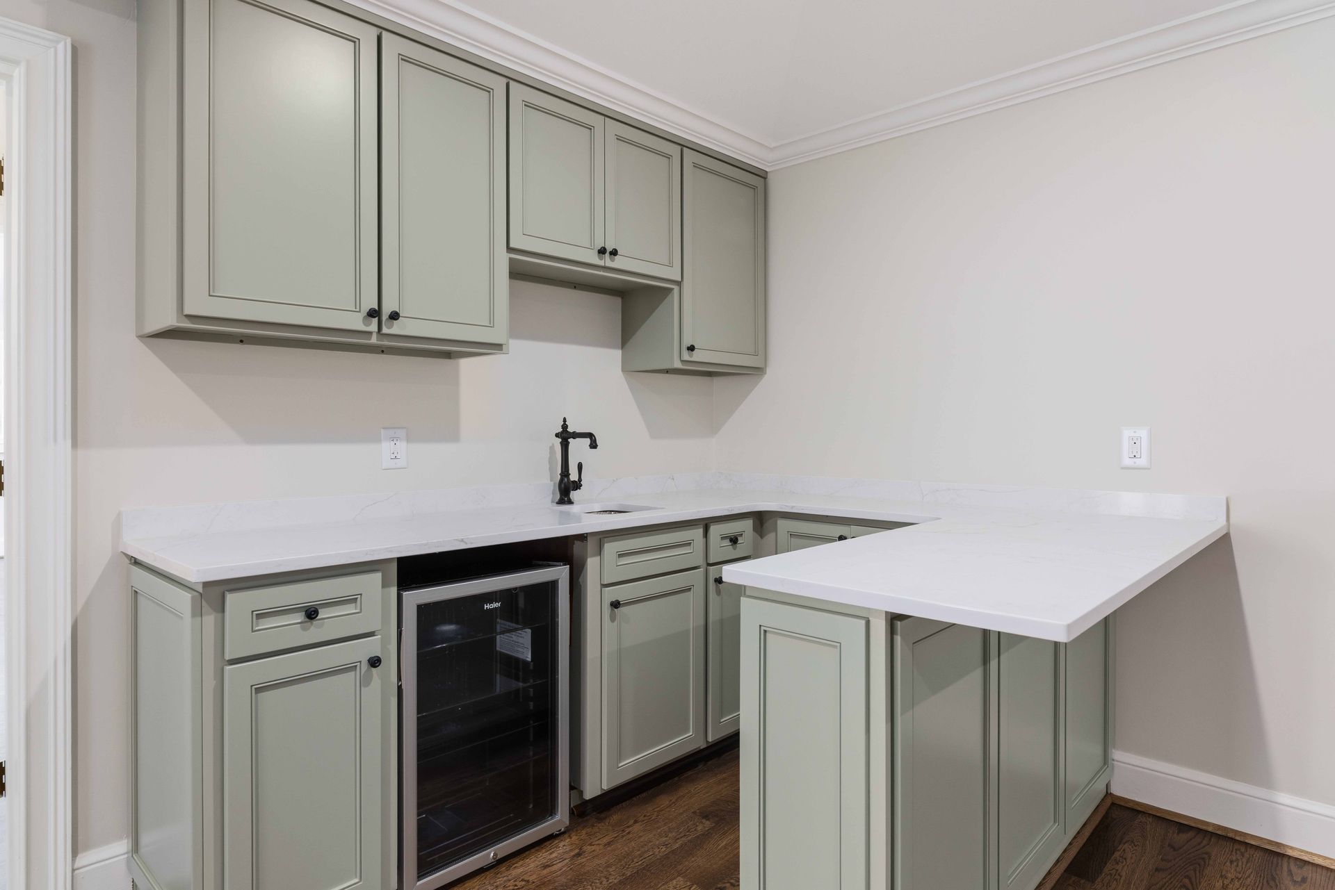 Compact kitchen with sage cabinets, black appliances, and a white peninsula counter