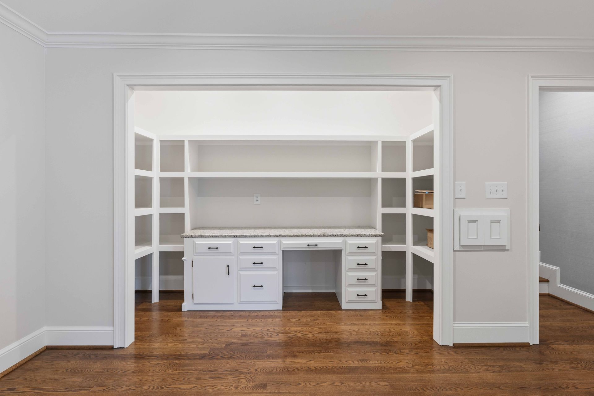 Empty white home office with built-in shelves and a white desk in a doorway-like alcove on hardwood floors
