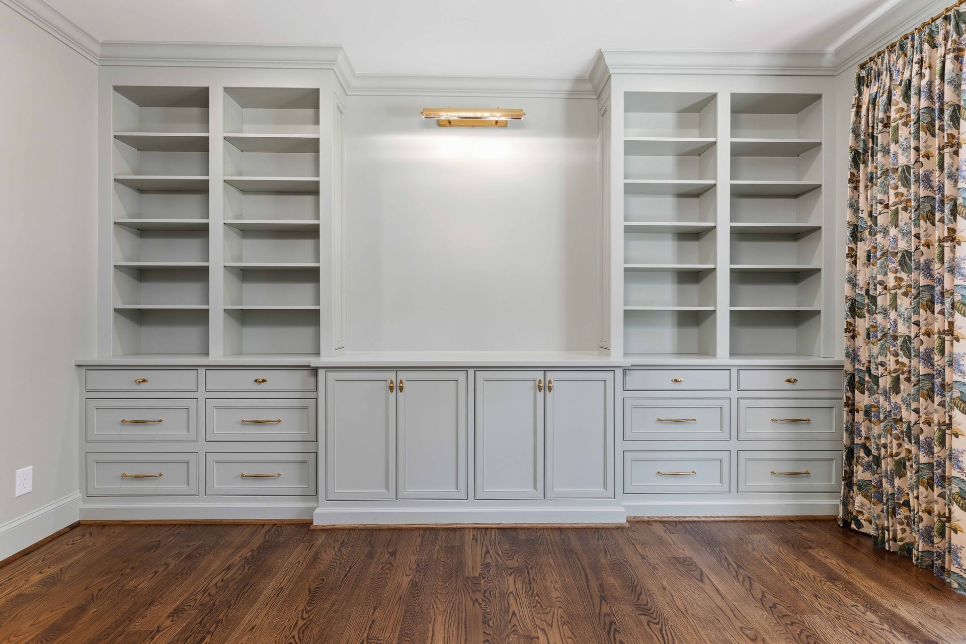 Built-in white shelving and cabinets flanking a central wall niche in a room with wood flooring