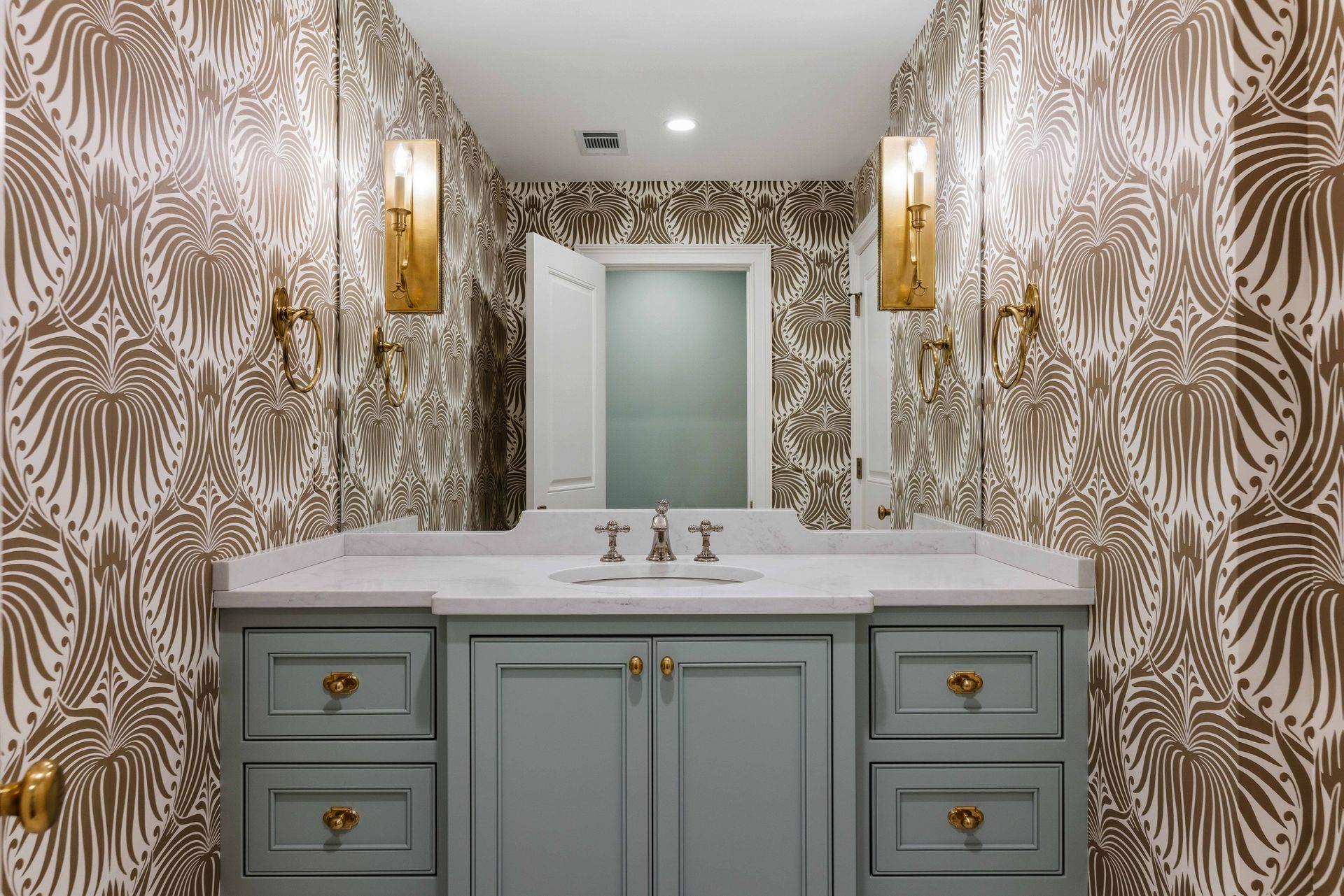 Elegant bathroom vanity with white countertop, gray cabinets, gold fixtures, and patterned wallpaper