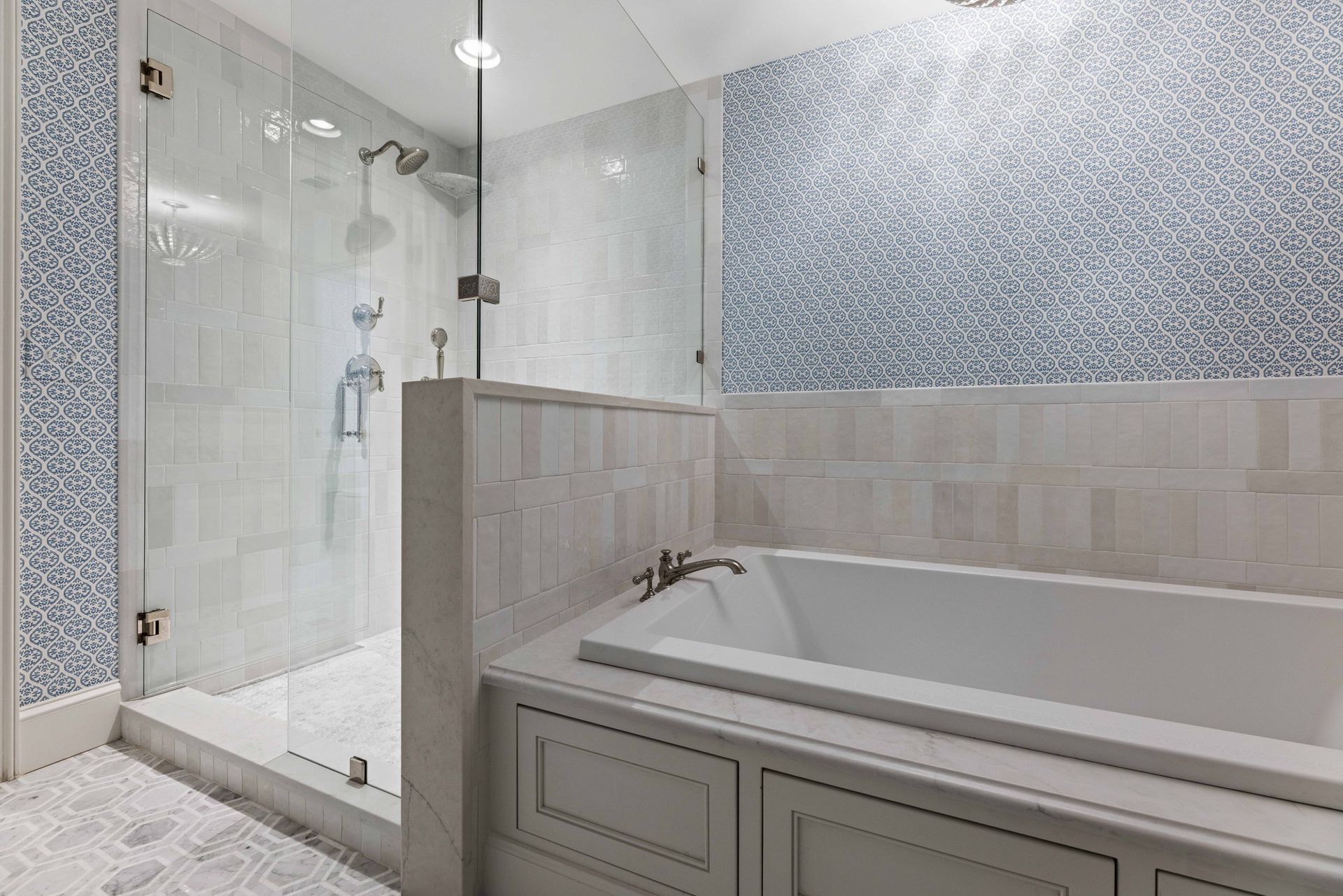 Modern bathroom with glass shower, white tub, and gray patterned tile accents