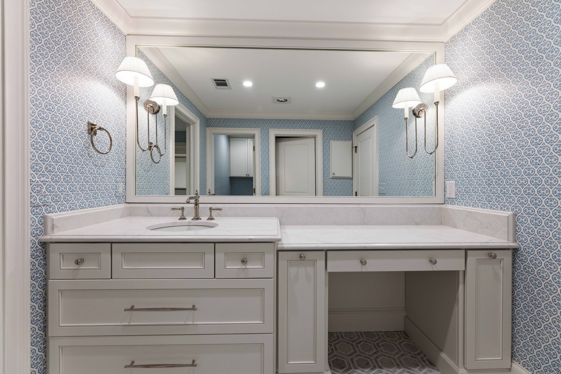 Elegant bathroom vanity with large mirror, white cabinets, and twin sconces in a blue patterned room