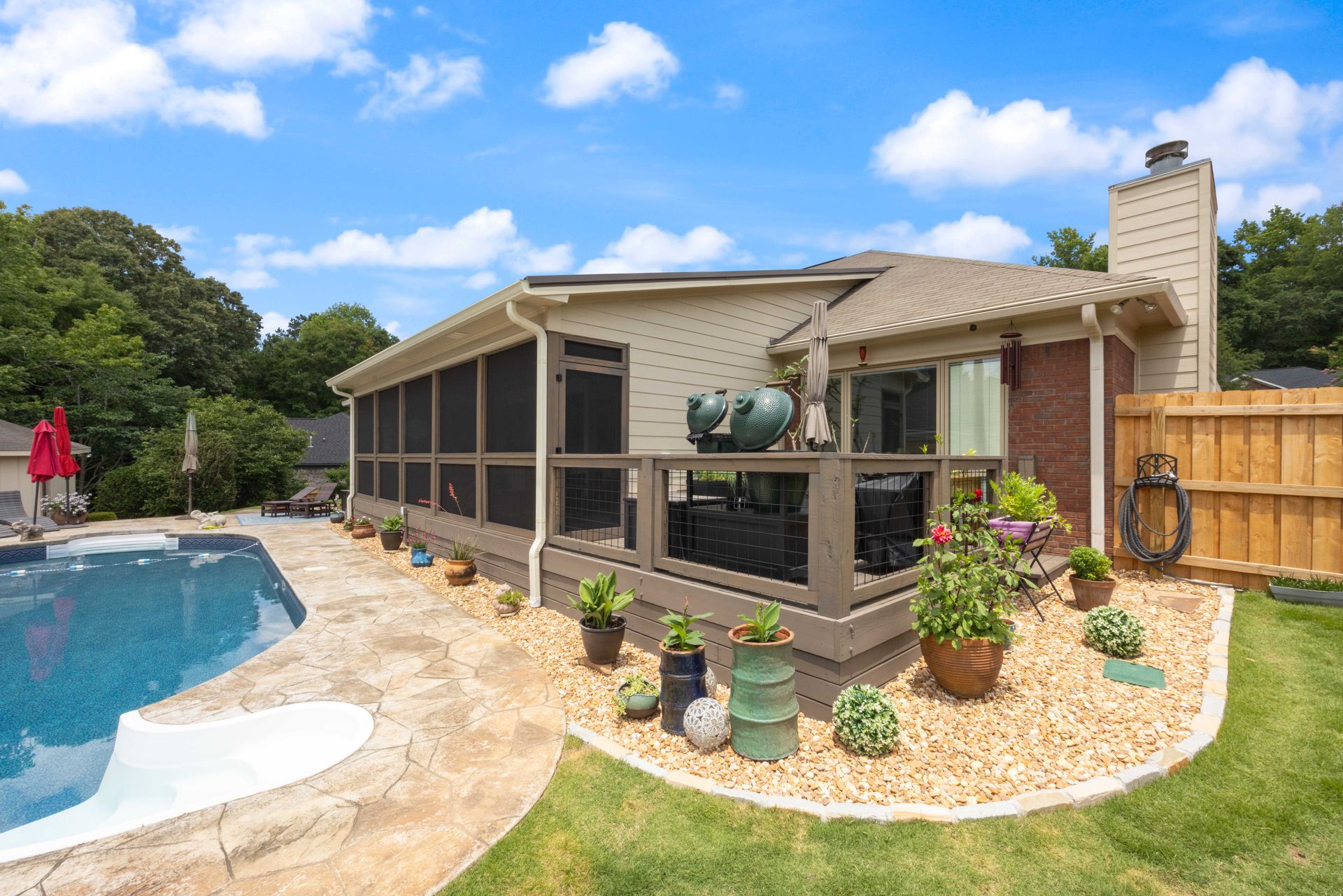 Backyard patio with pool, screened porch, grill, and potted plants beside a brick house