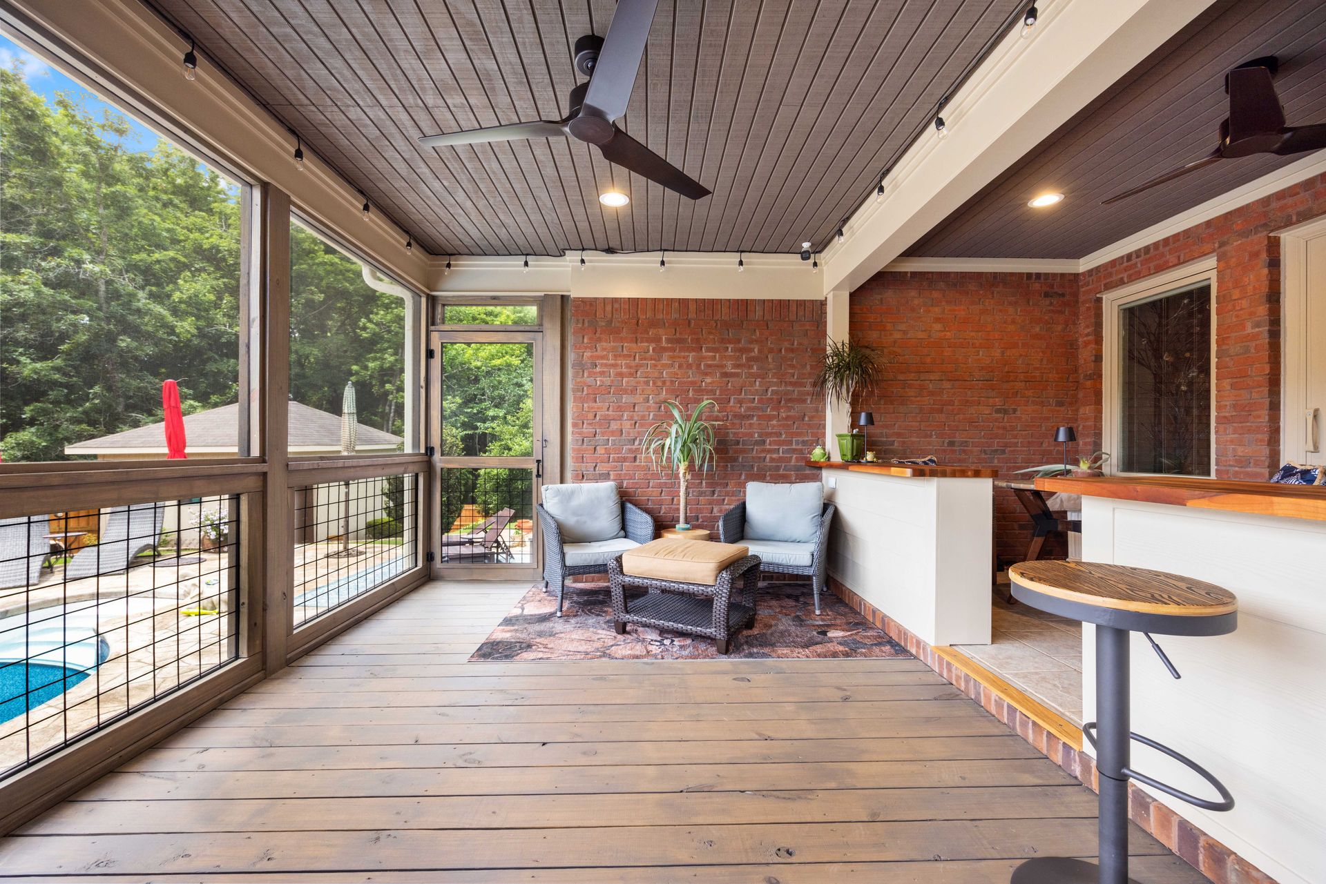 Covered patio with brick wall, wood ceiling fan, seating area, bar, and a view of the pool.