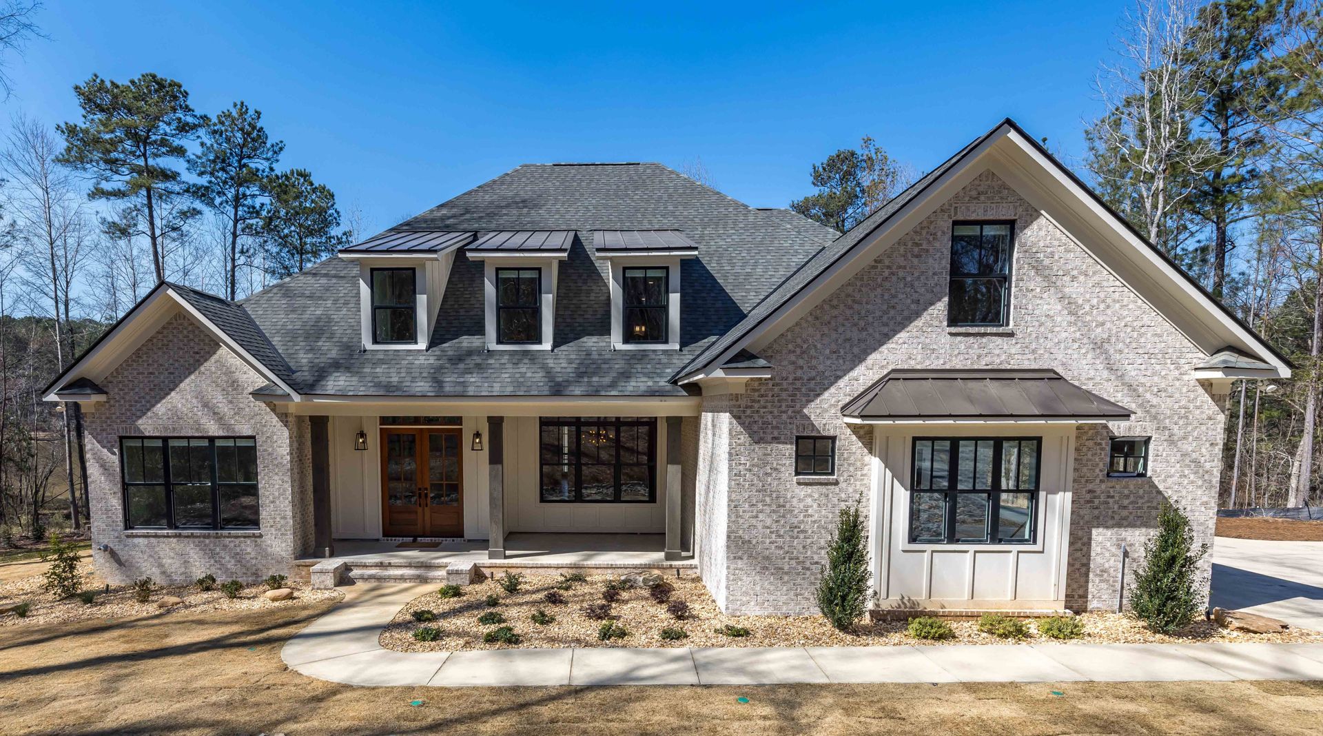 Large modern brick house with a front porch, dormer windows, and a landscaped yard