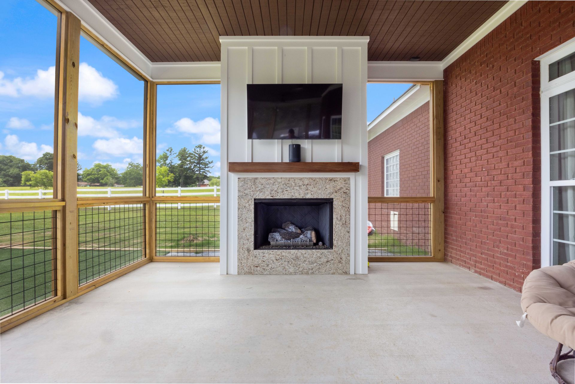 Covered patio with a fireplace, TV, and screened railing overlooking a grassy yard