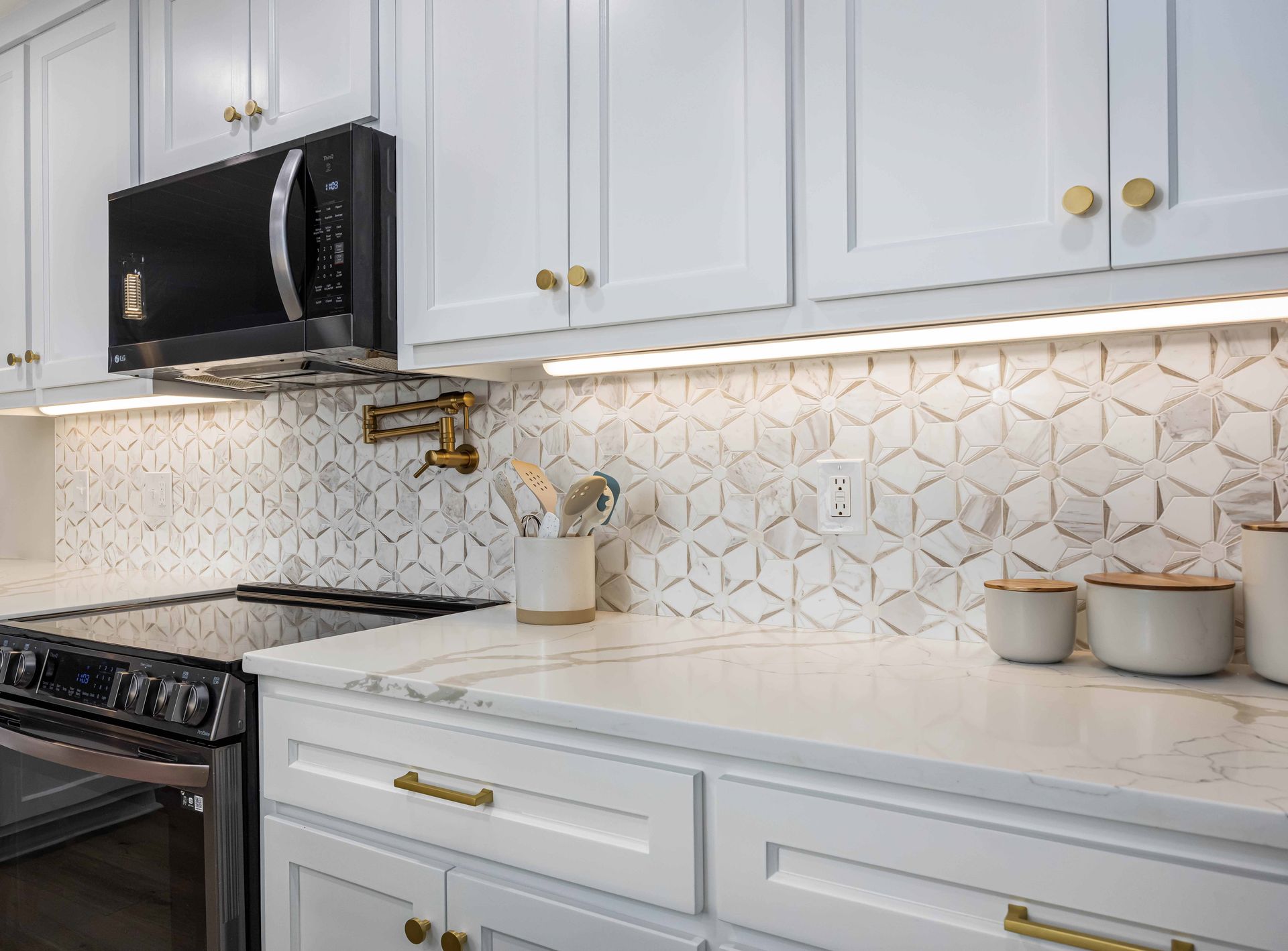 Bright white kitchen with geometric tile backsplash, black microwave, and white cabinets with gold handles