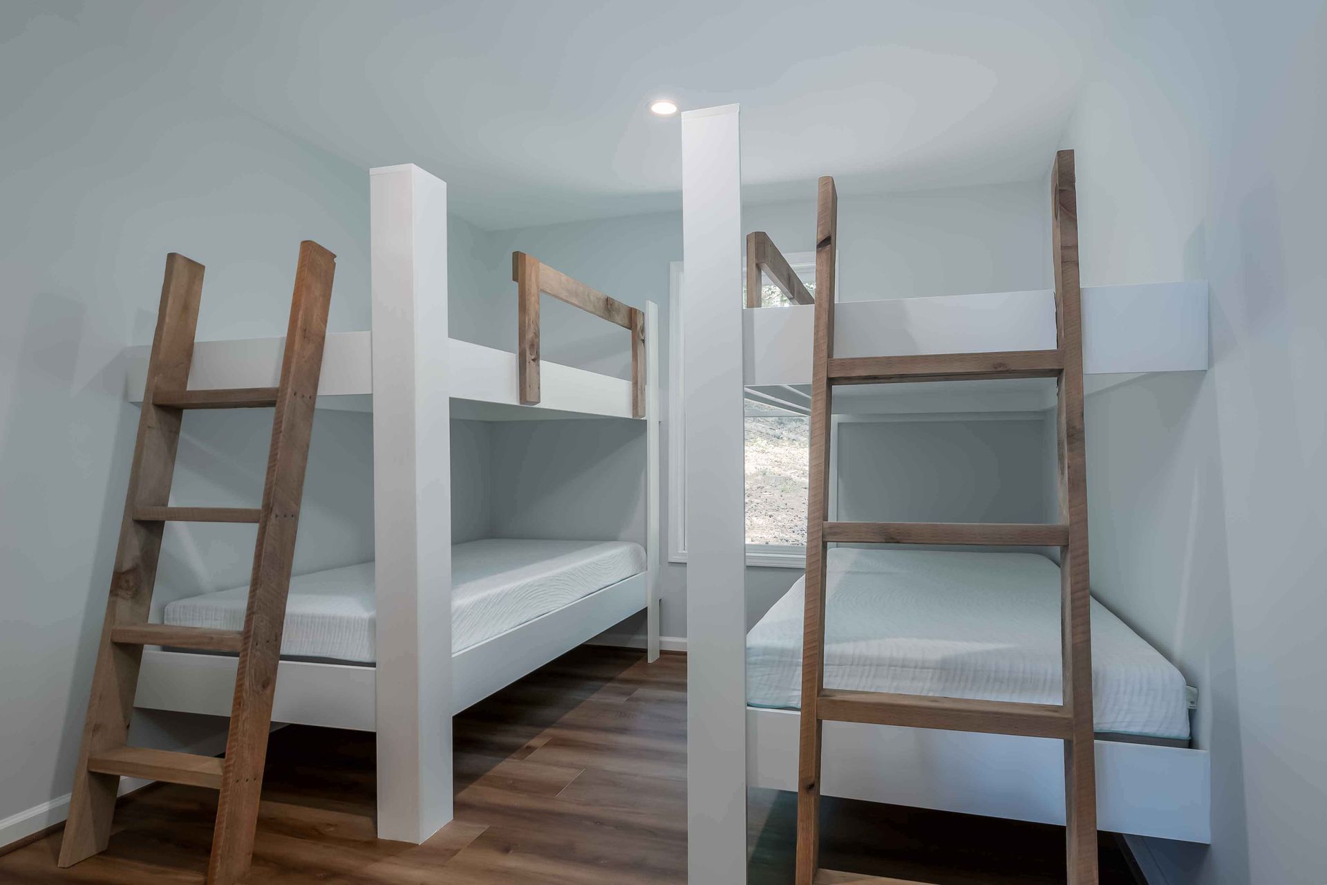 White bunk beds in a loft bedroom with wooden ladders on both sides.