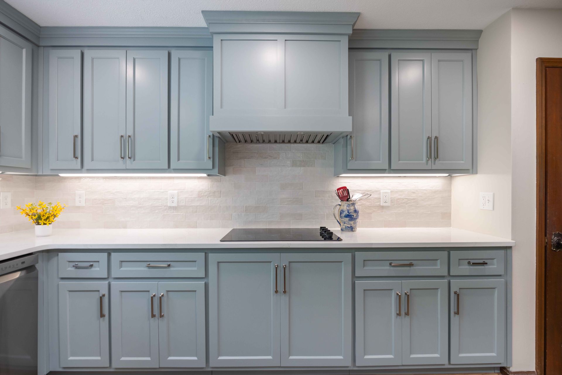 Light blue kitchen cabinets with white countertops, a stove, and a tiled backsplash.