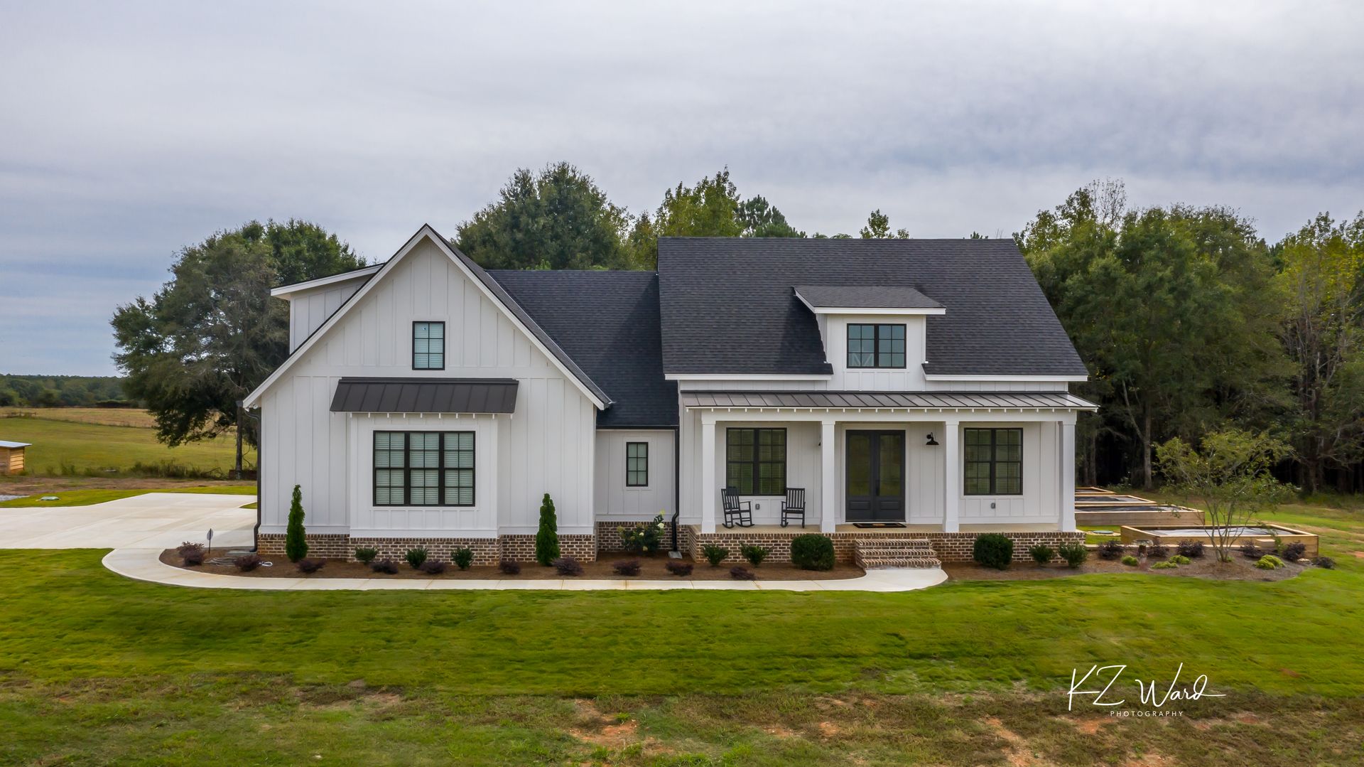White farmhouse with dark roof and front porch in a grassy rural setting