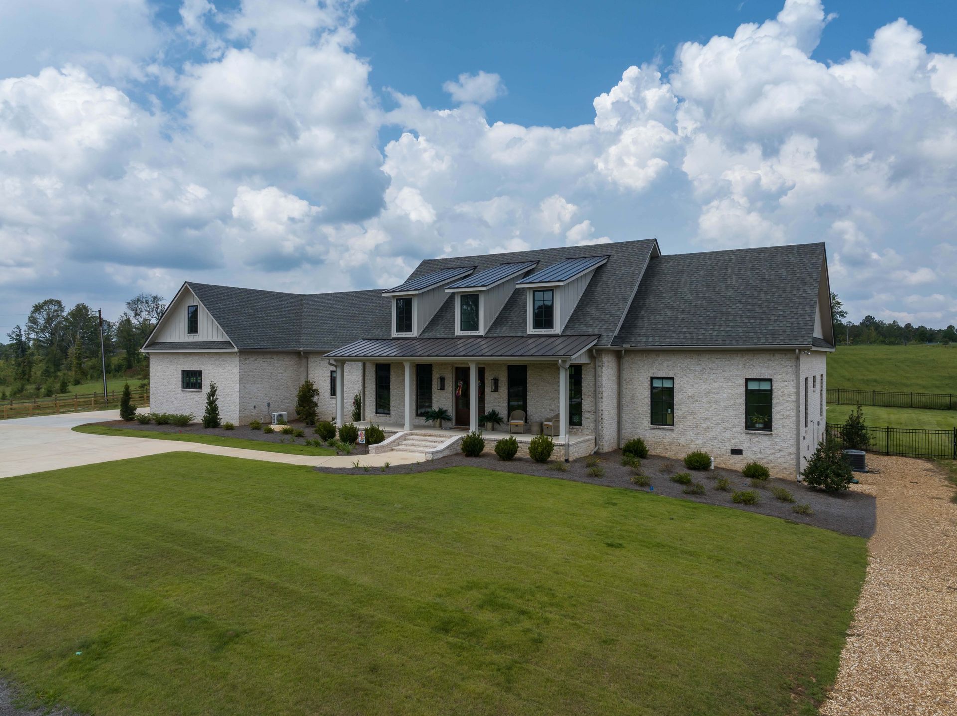 Large white house with a dark roof, front porch, and wide green lawn under a cloudy sky