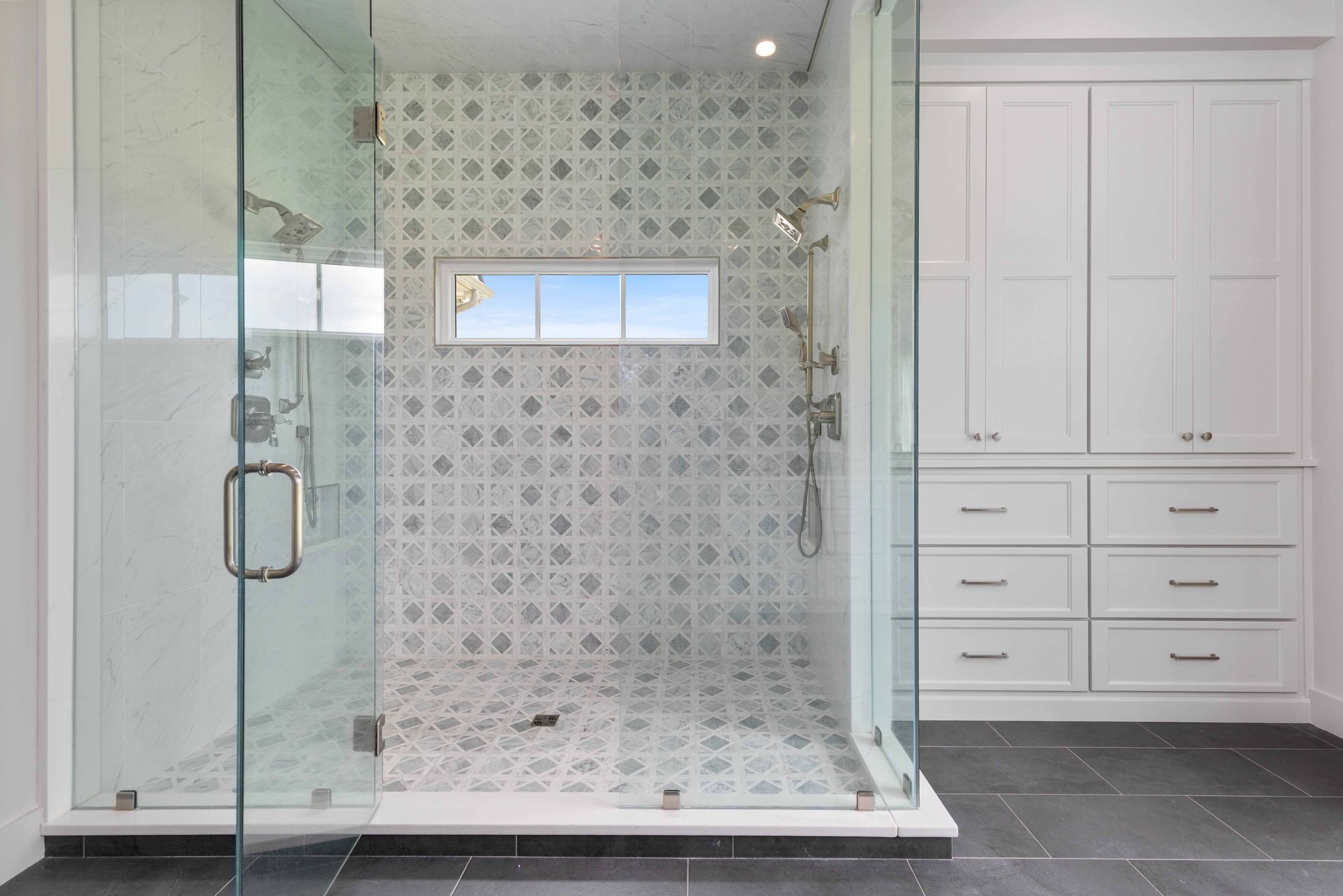Modern bathroom with glass-enclosed shower, patterned tile, and white built-in cabinets