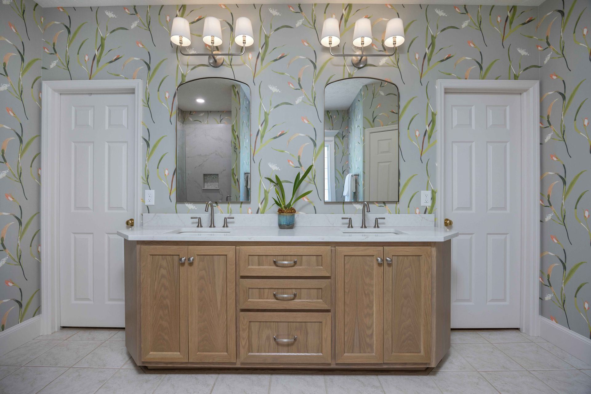 Modern bathroom with double sinks, wood vanity, mirrors, and floral wallpaper