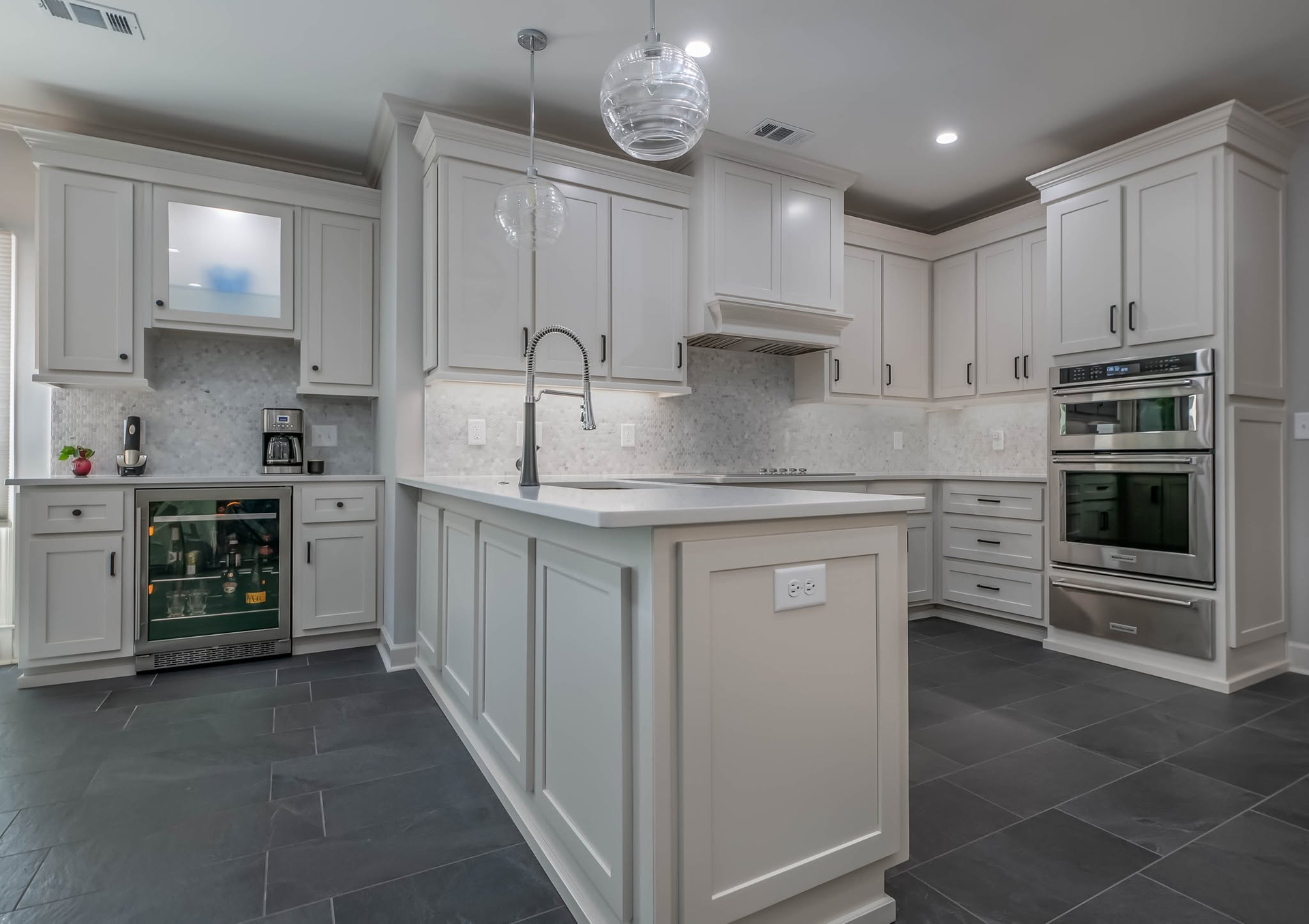 Bright white modern kitchen with island, marble counters, dark floor, and built-in ovens