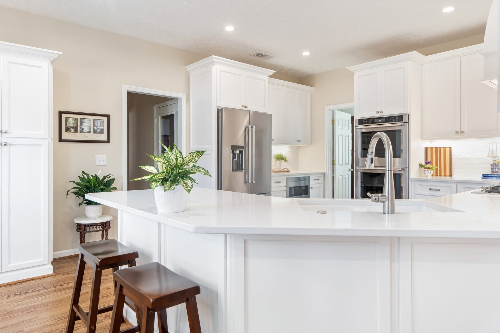 Bright white kitchen with island, stools, stainless steel appliances, and a potted plant