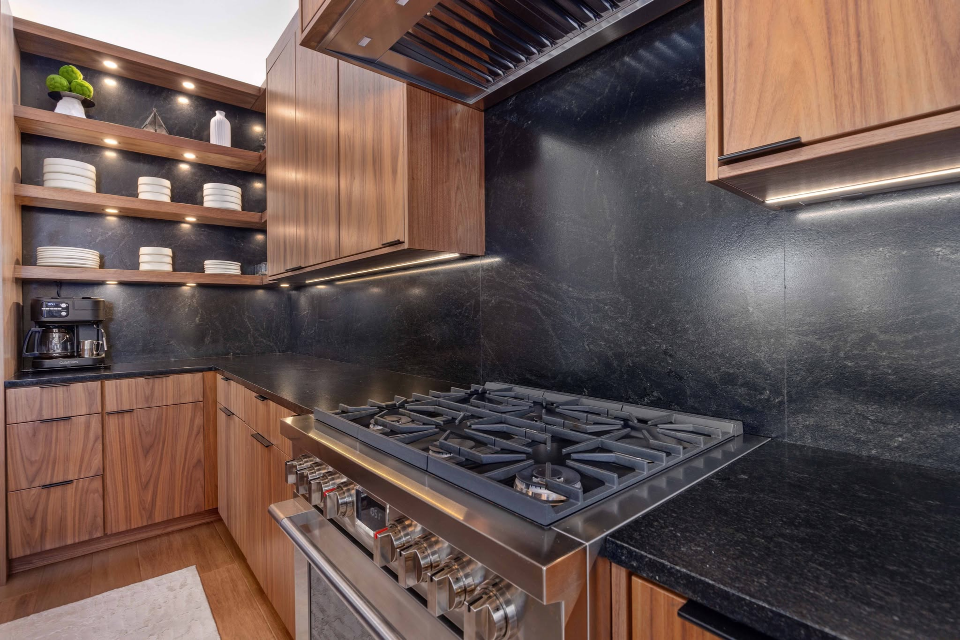 Modern kitchen with wood cabinets, black countertops, stainless range, and open shelves