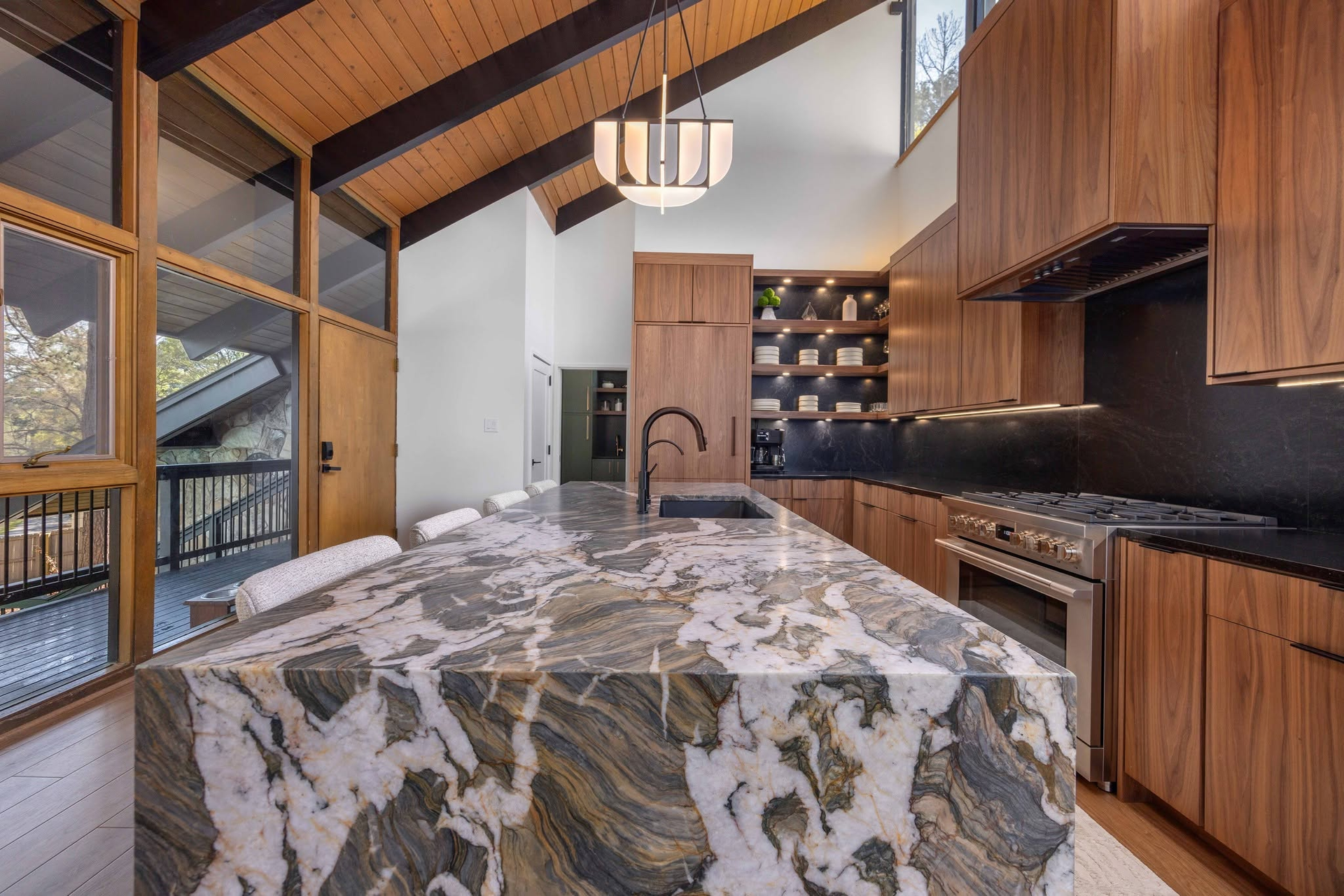 Modern kitchen with wood ceilings, stone island, and large windows overlooking a deck