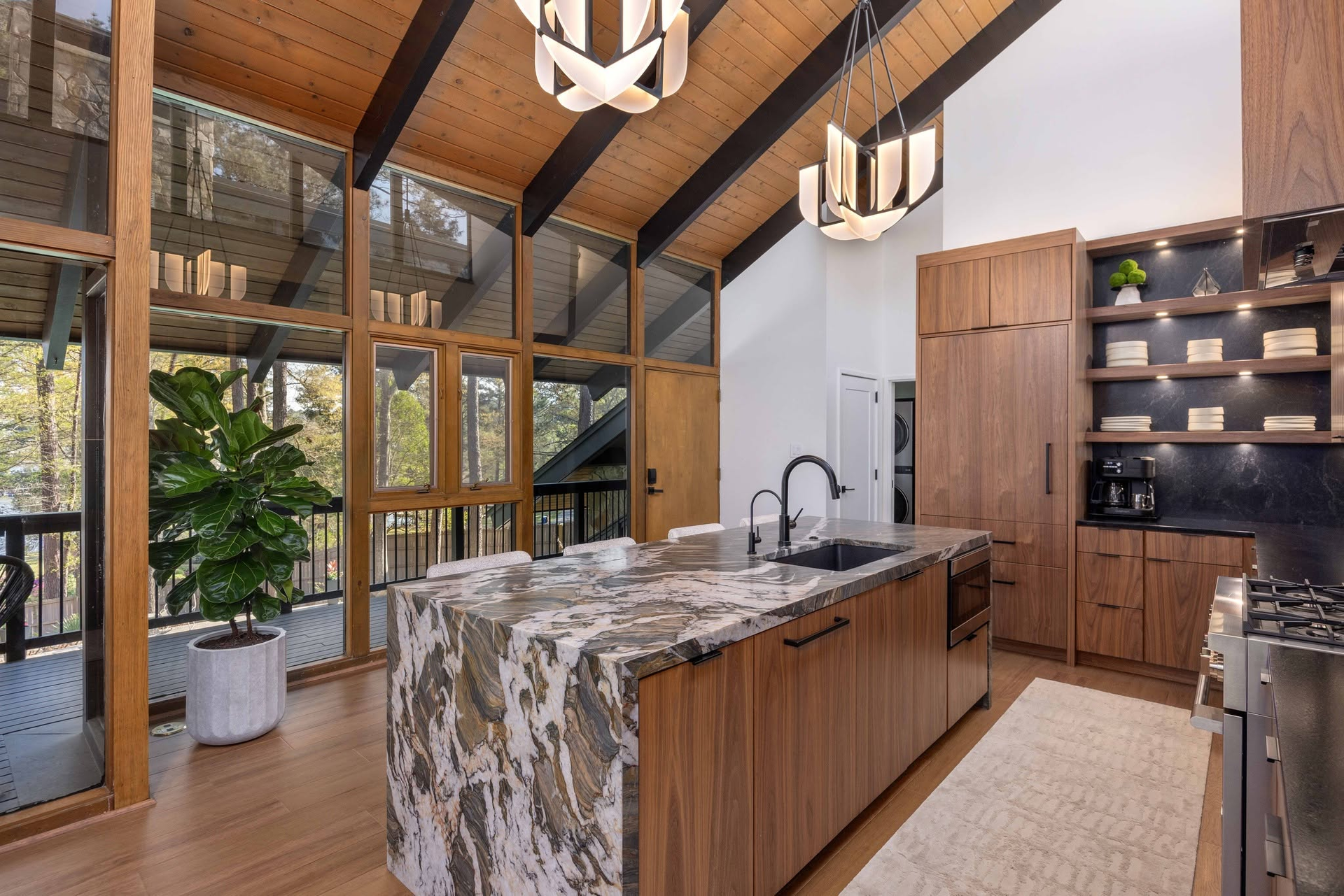 Modern rustic kitchen with wood beams, marble island, black fixtures, and large windows.