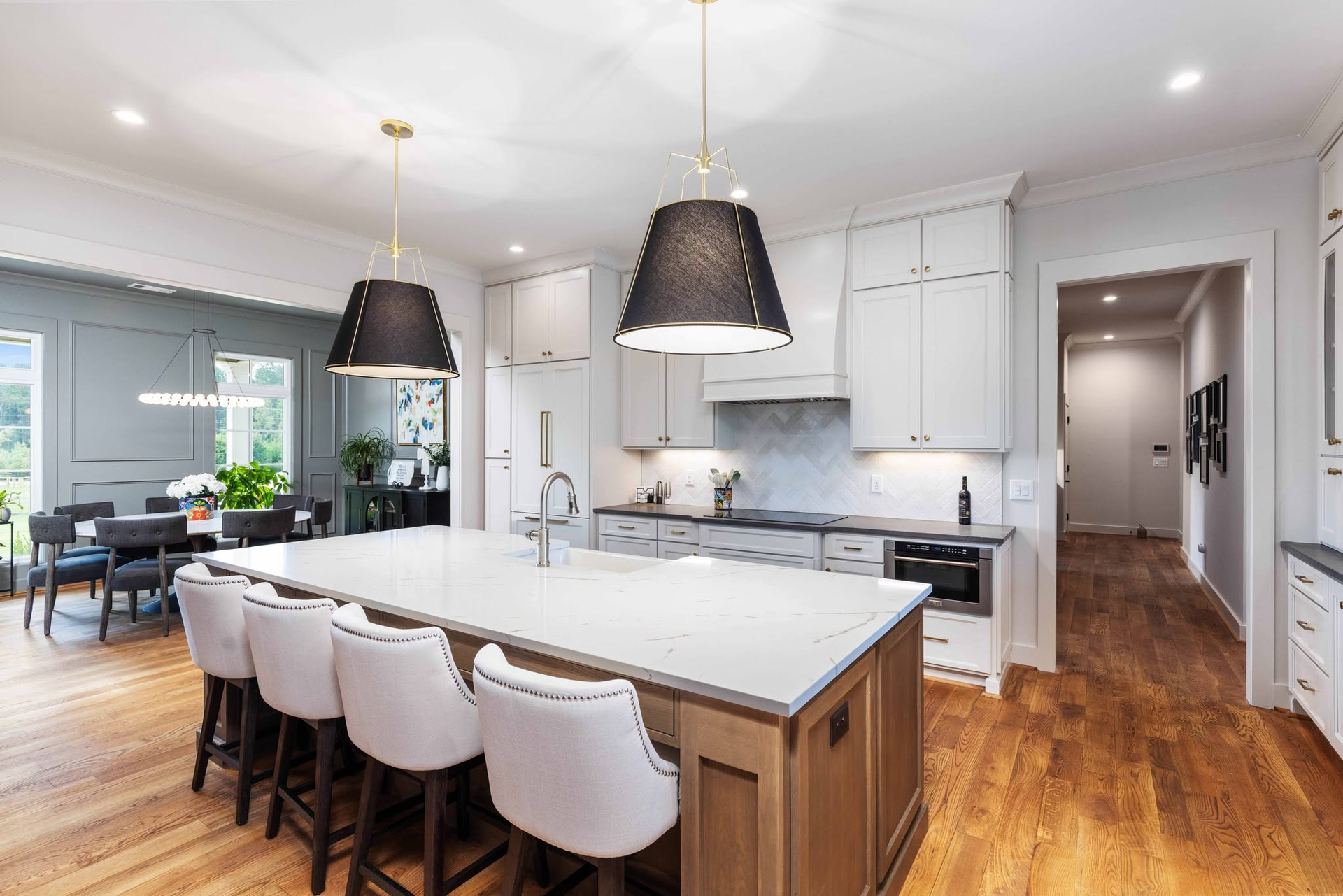 Bright kitchen with white cabinets, island seating, black pendant lights, and hardwood floors