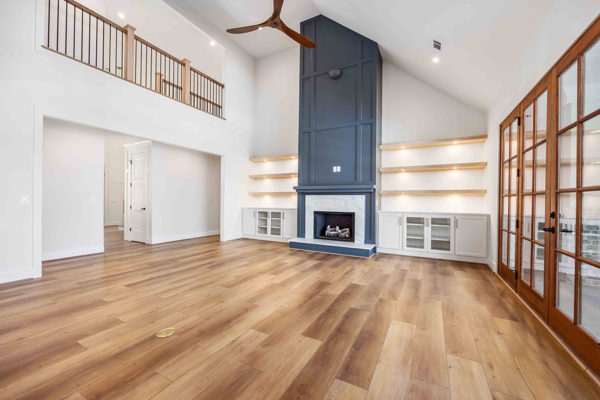 Bright open living room with hardwood floors, vaulted ceiling, fireplace, and glass-paneled doors