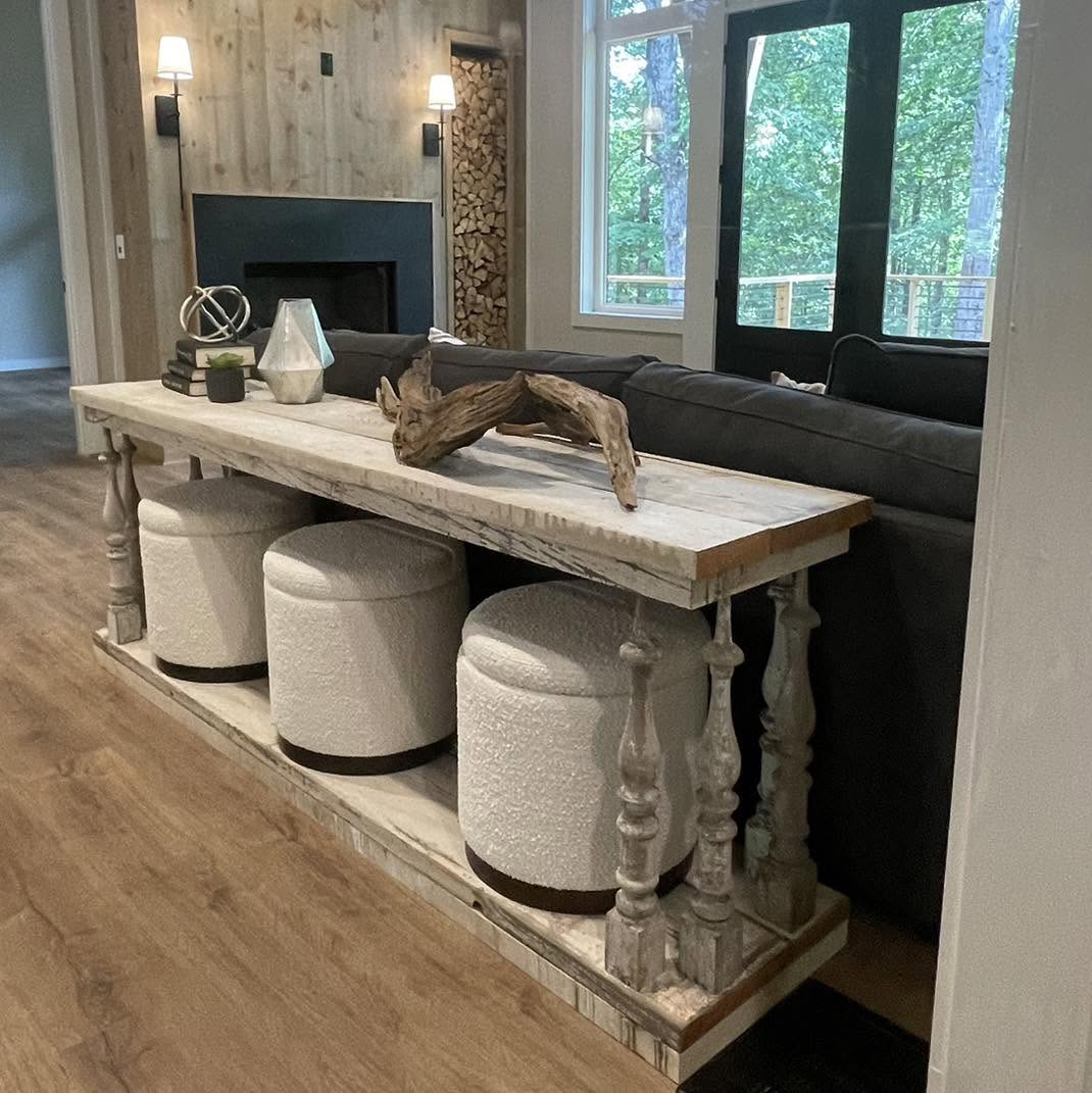 Modern living room with fireplace, large windows, long console table, and two white ottomans