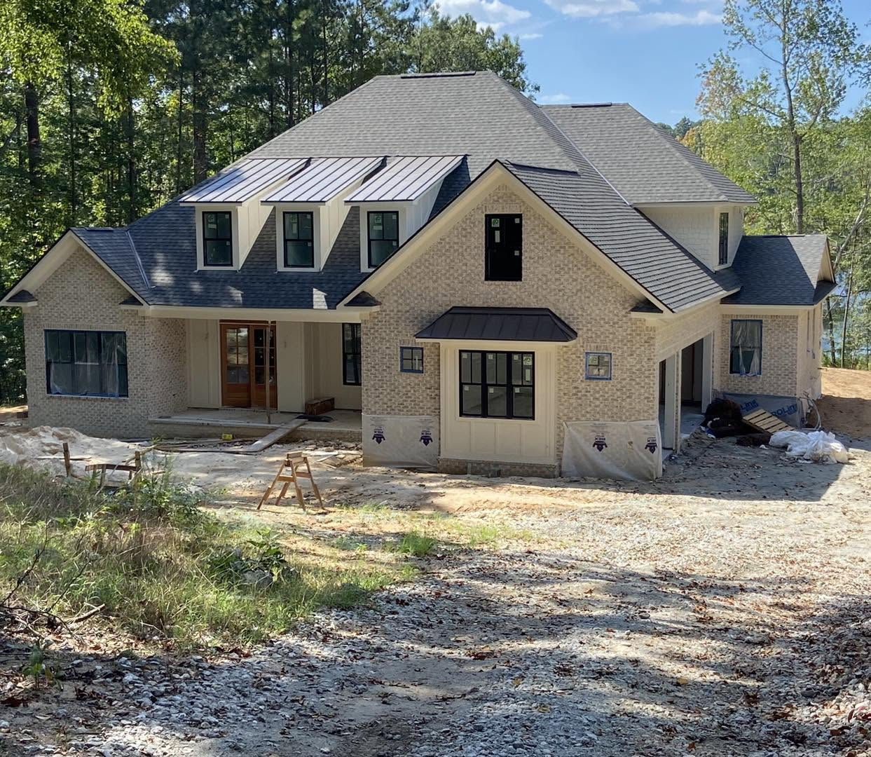 New brick house under construction surrounded by trees and gravel driveway