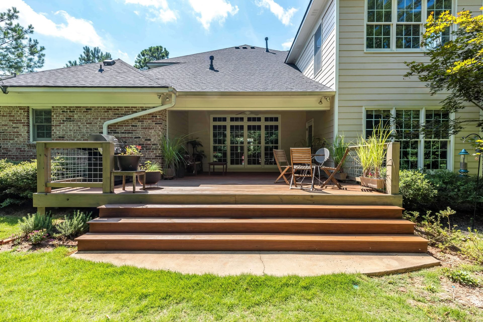 Backyard patio with wooden steps, covered seating area, and large house windows