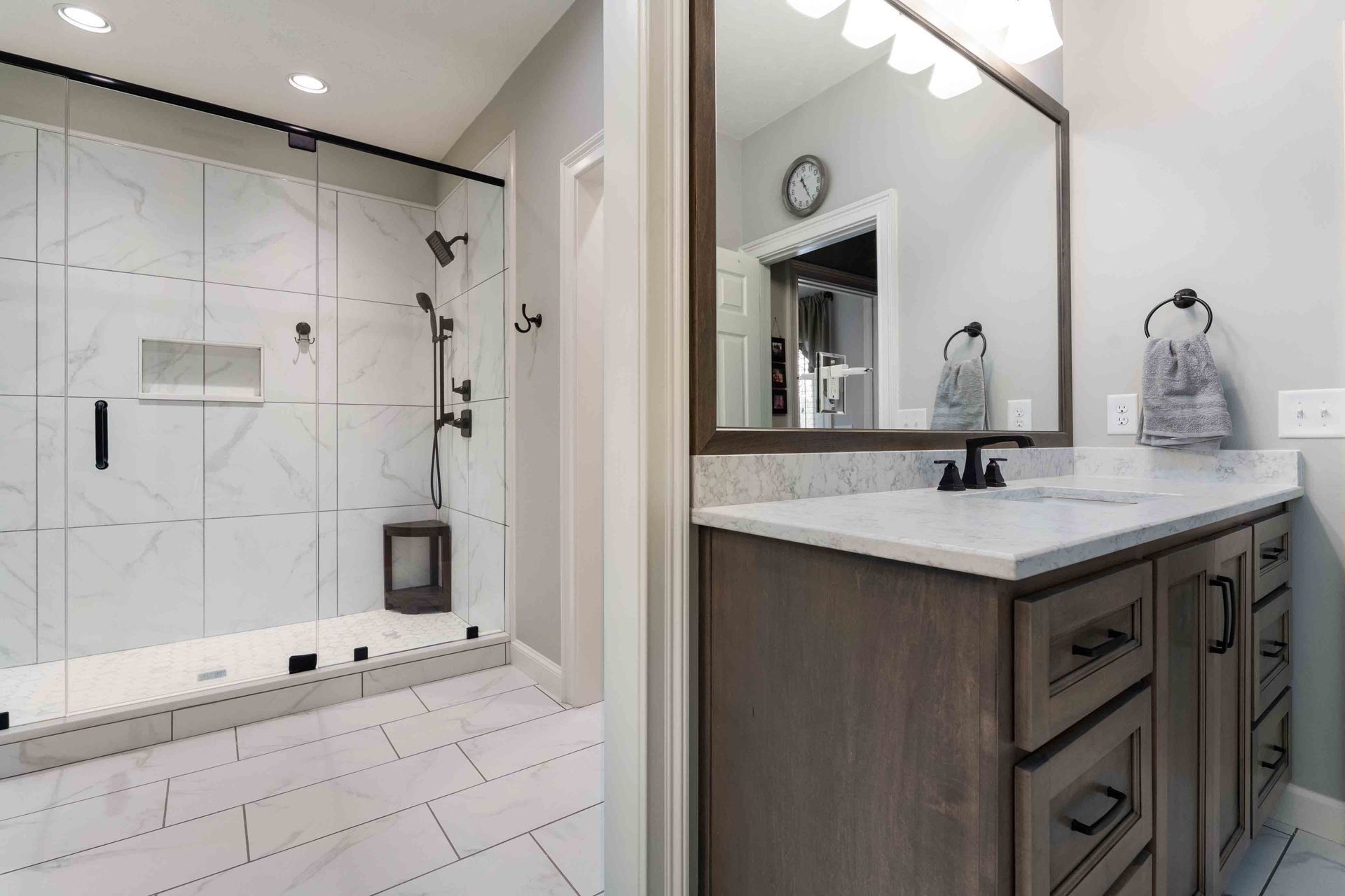 Modern bathroom with tiled walk-in shower, white vanity, large mirror, and marble countertop