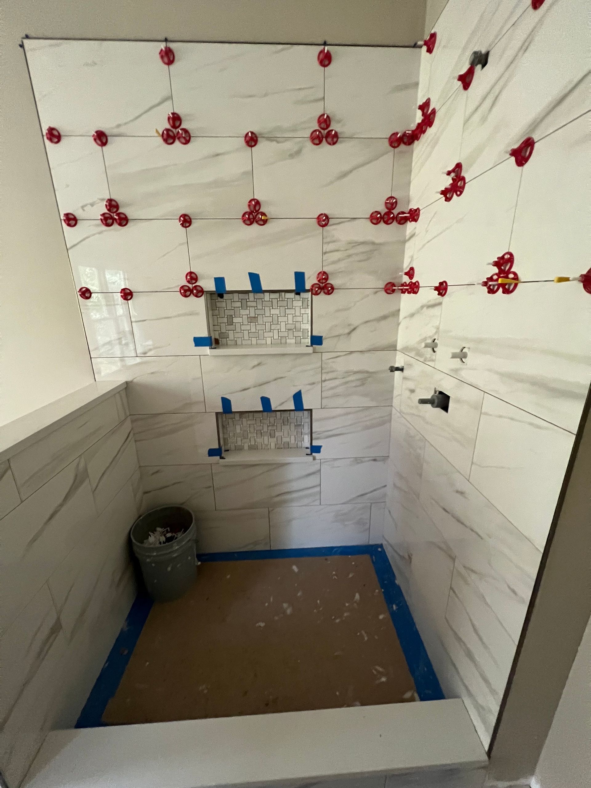 Partially tiled bathroom under renovation, with blue tape, unfinished walls, and a toilet alcove.
