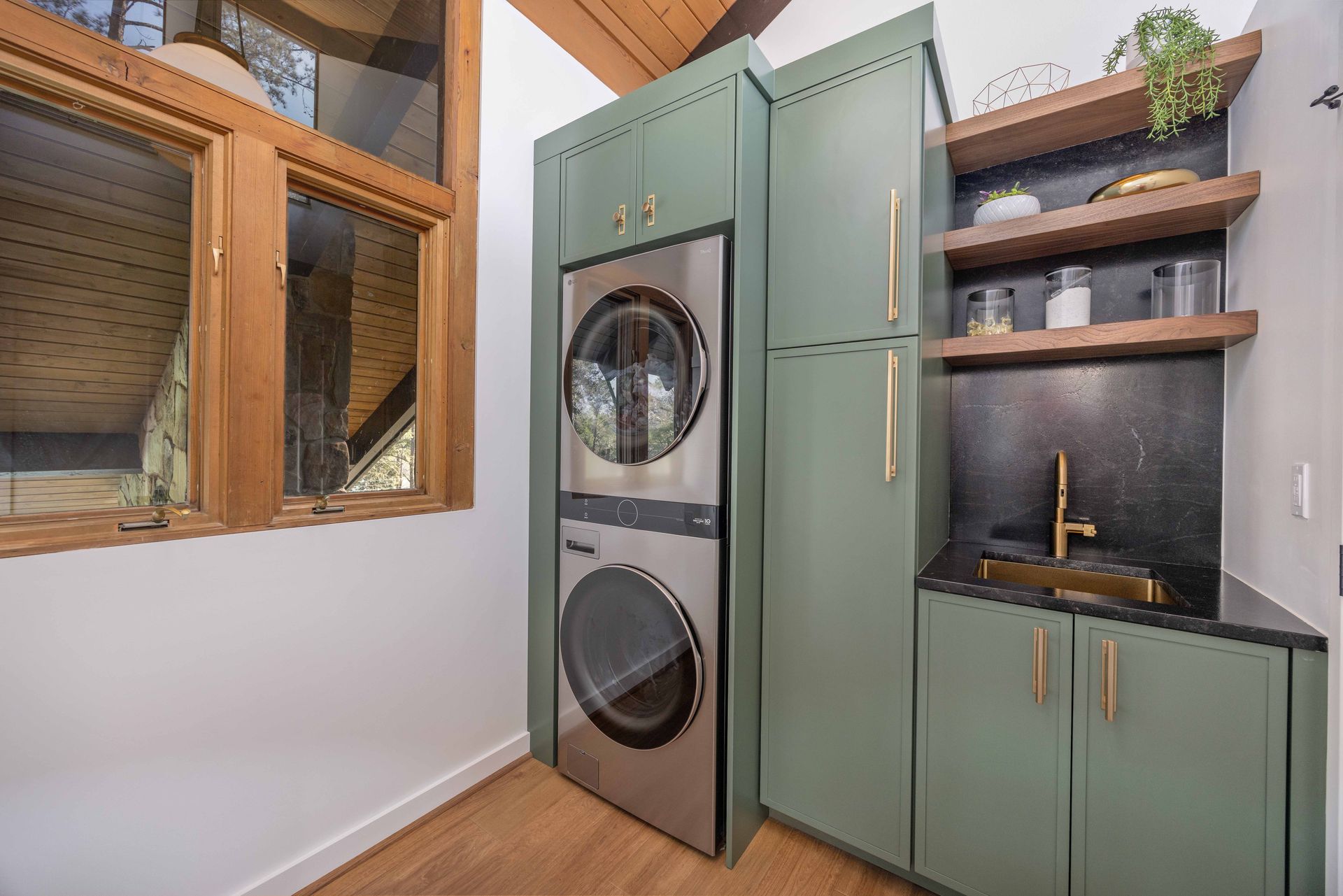 Laundry room with stacked washer-dryer, sage green cabinets, wood shelves, and a sink